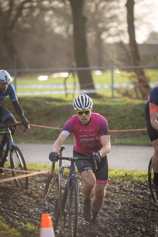 A man riding a blue bike wearing pink and black. He is wearing a helmet with the word "Gator" on it.