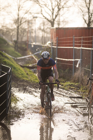 A cyclist is riding in a muddy area near some fencing, under the words cyclocross and masters.