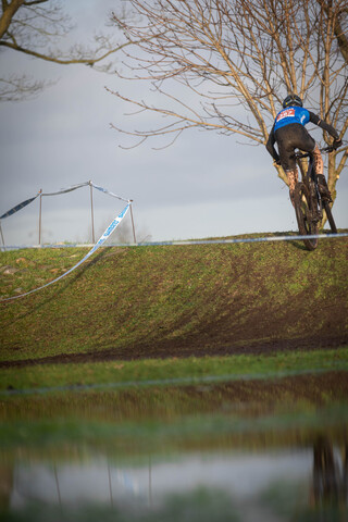 Cyclocross racer, number 7, jumping over a hurdle on a mountain of dirt.