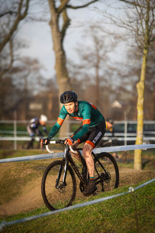 A cyclist with a green and black jersey is riding their bike on grass. The rider has the number 12 on their jersey.