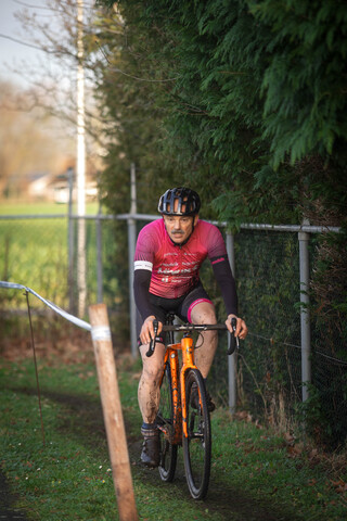 A man wearing a pink shirt is riding his orange bike.