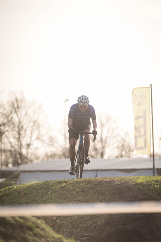 A man in a blue shirt and black shorts is riding his bike on the track of the Cyclocross Masters 2023 race.