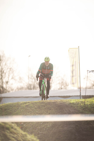 A man in a green jersey is riding a bike on a grassy hill.