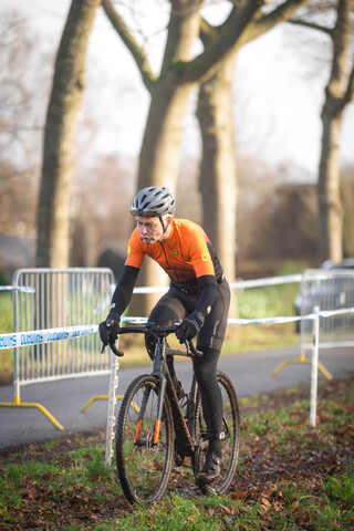 A young man wearing a black and orange cycling outfit rides his bike through a small field in the Netherlands.