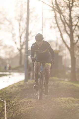 A man in a black and yellow cycling uniform is riding a mountain bike on a muddy path. He has the word "Giant" on his jersey.