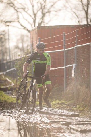 A cyclist wearing a yellow and blue jersey that says Masters on the front rides his bike through a muddy area.