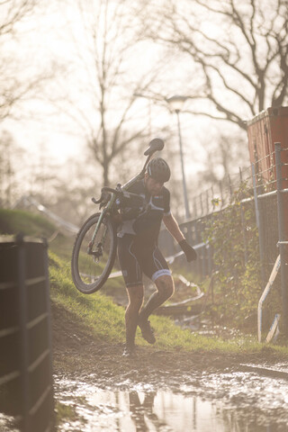 A person carrying a bicycle while wearing a helmet.