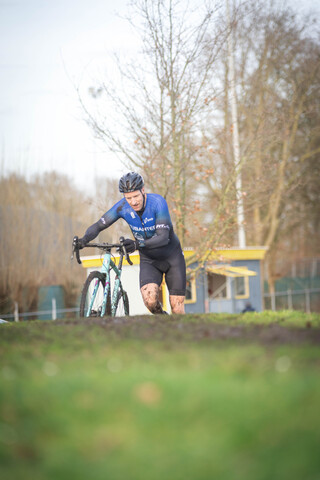 A man is riding a bike in a field. The background has a yellow building and a sign with the letters "GOW".