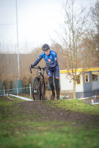 A cyclist wearing a blue and white jersey is standing with his bike.