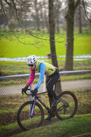 A person wearing a pink shirt and a blue helmet rides a purple bicycle.