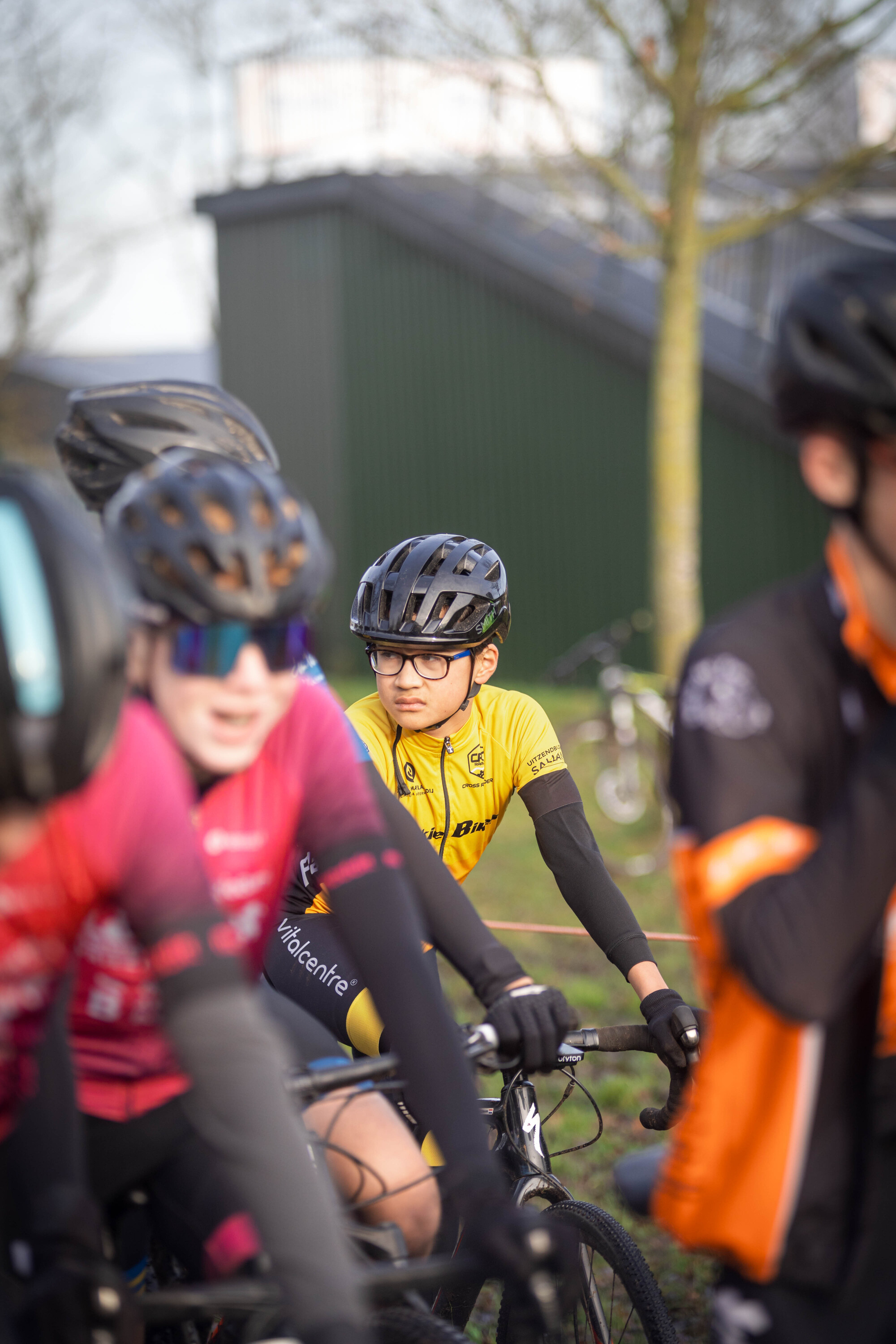 A group of cyclists in a race with one wearing sunglasses and a helmet.