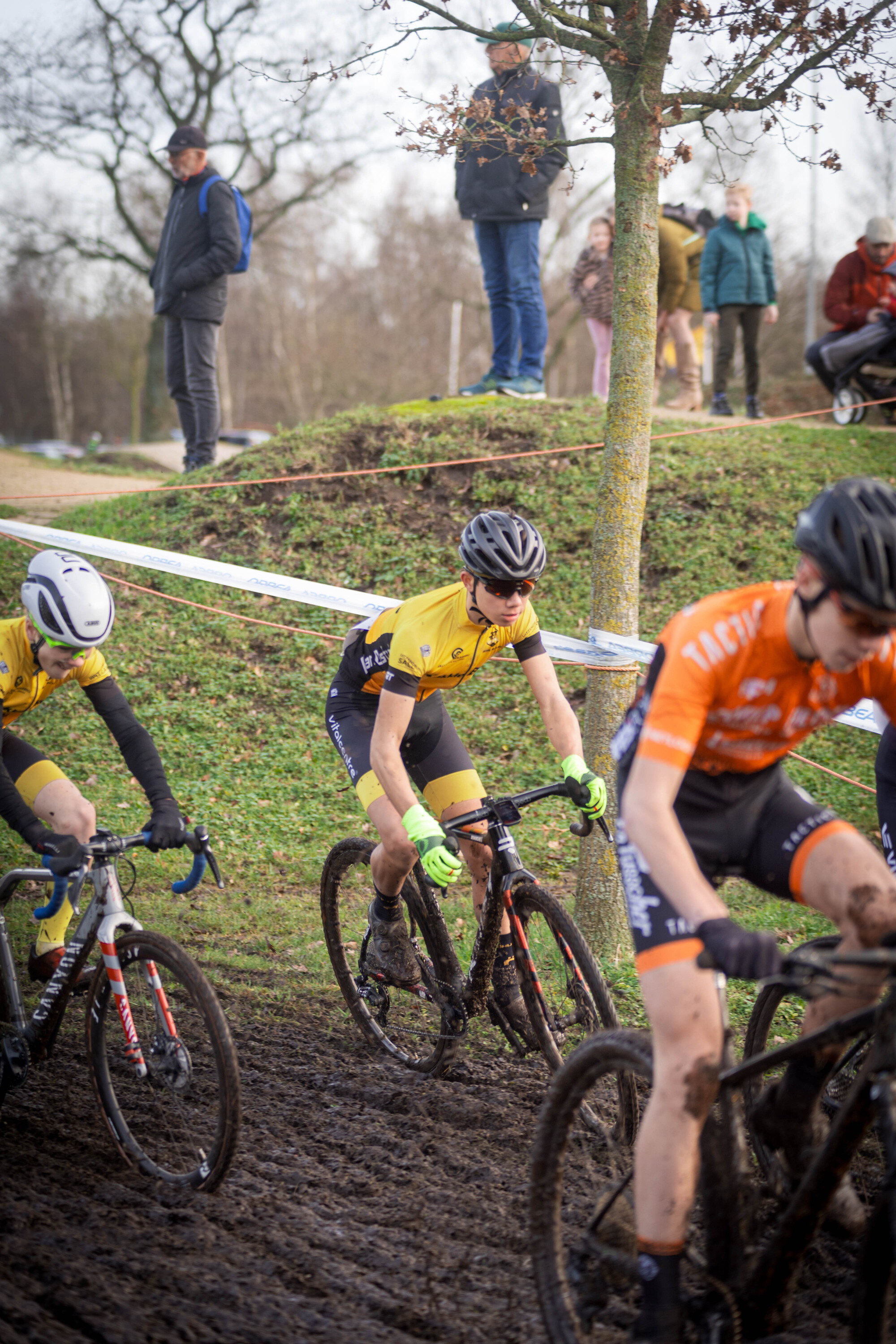 Four men are riding bicycles in a muddy area, and they have number 1 through number 4 on their shirts.