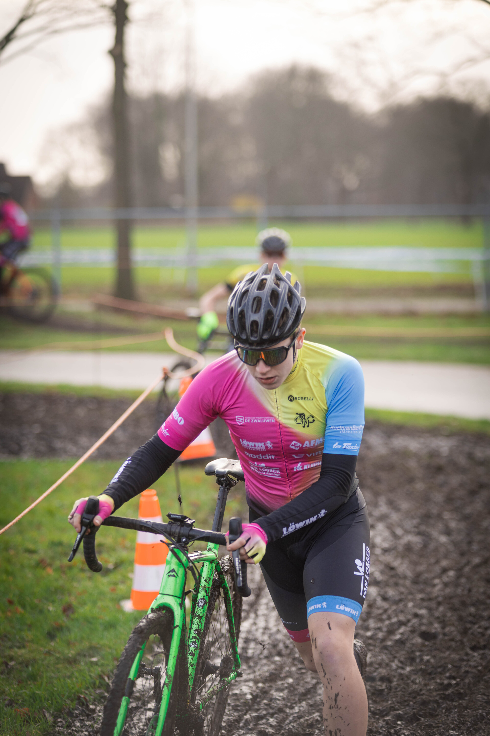 Cyclist in a blue and yellow jersey on a green bike. The cyclist has the number 6 on his shirt and a black helmet.