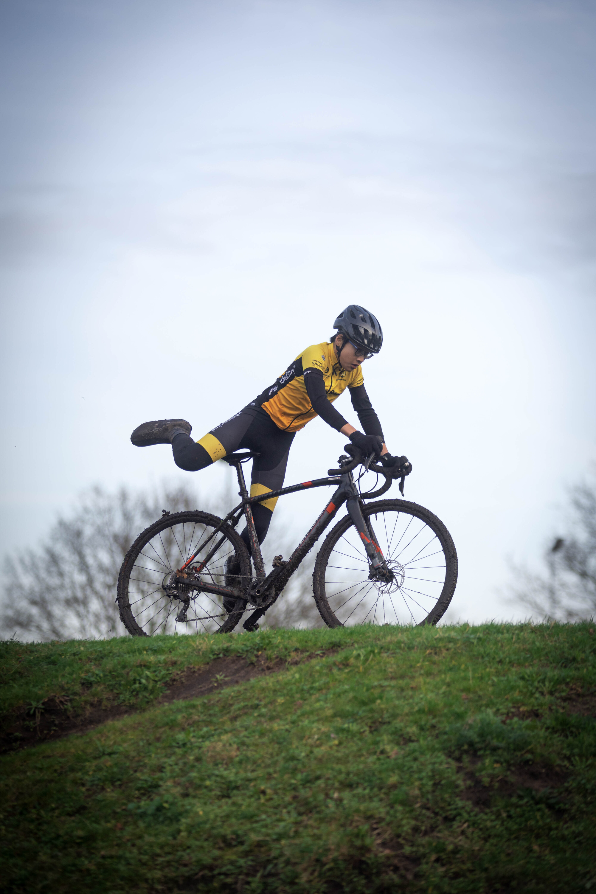 A man in a black and yellow striped shirt is riding his bike down a grassy hill.