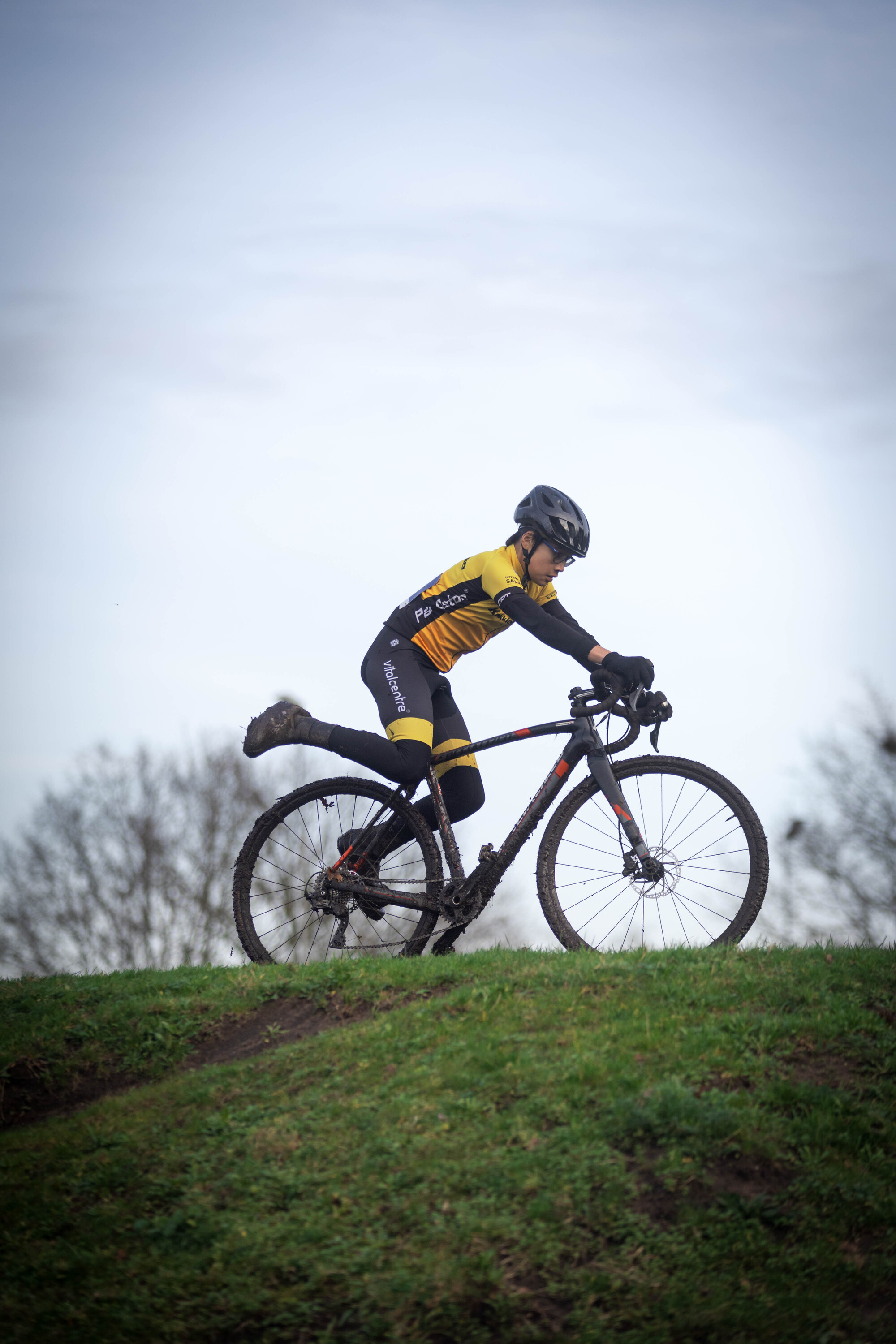 A woman in a black and yellow cycling outfit riding a bicycle on a hill.