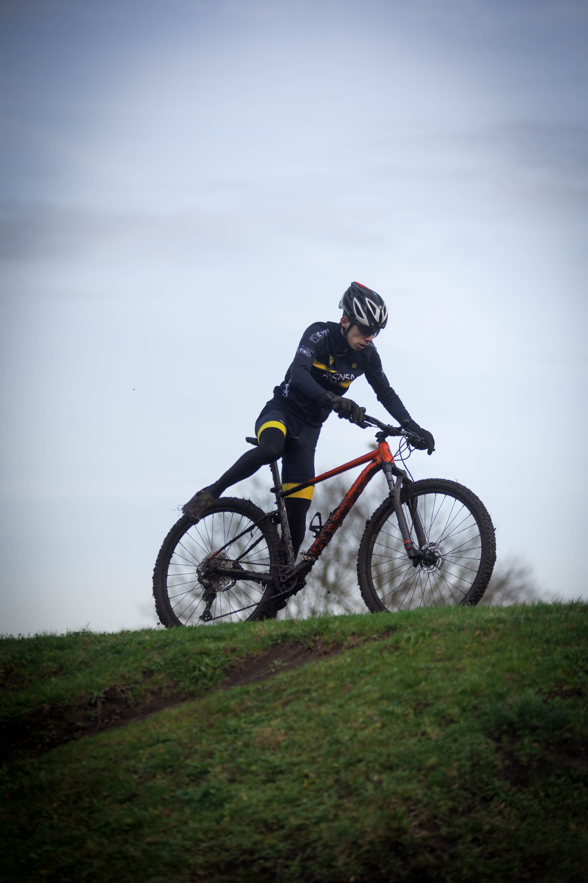 A man wearing a black suit is riding a red and yellow bike up a hill.