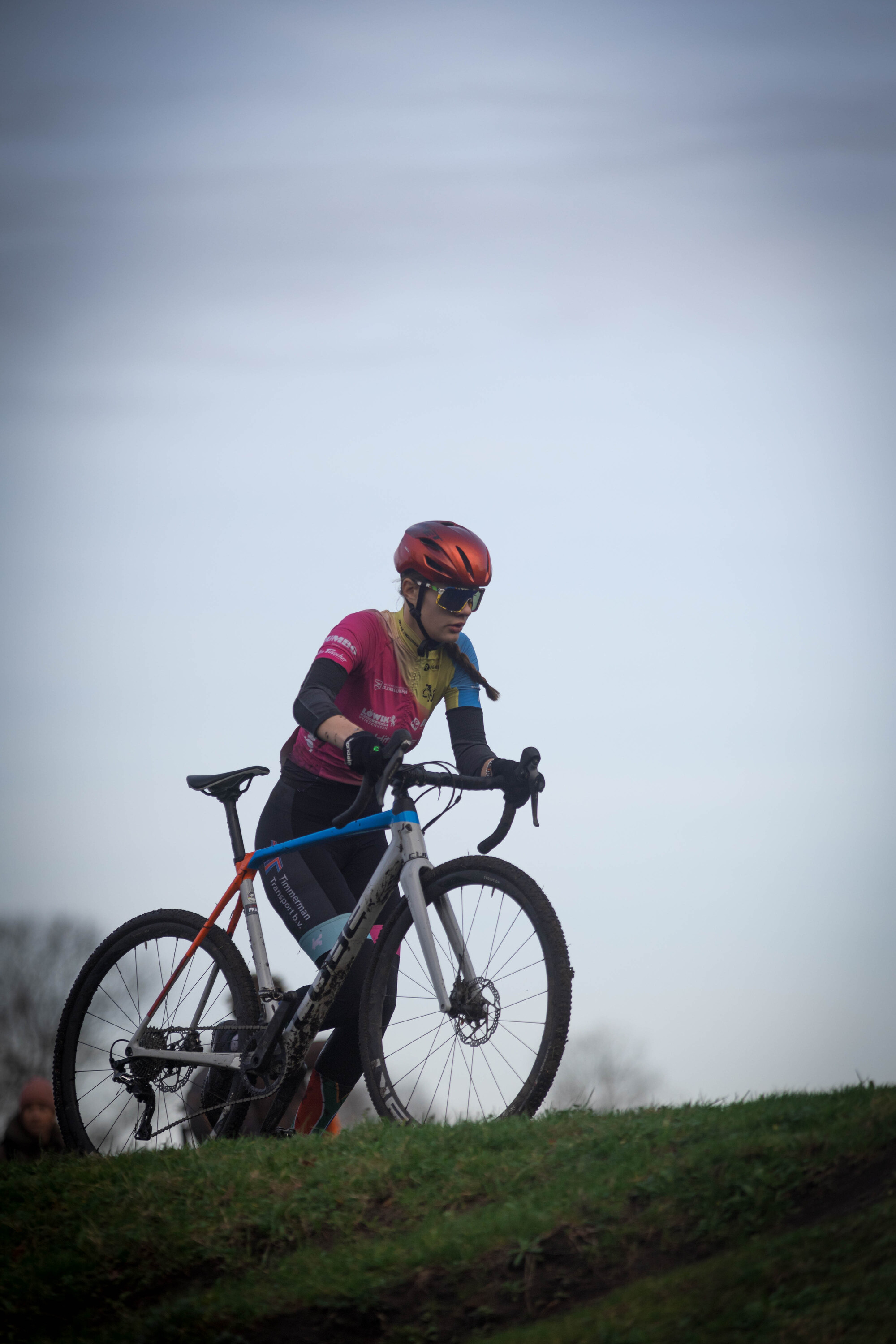 A man in a pink jersey and red helmet rides his bike on a hill.