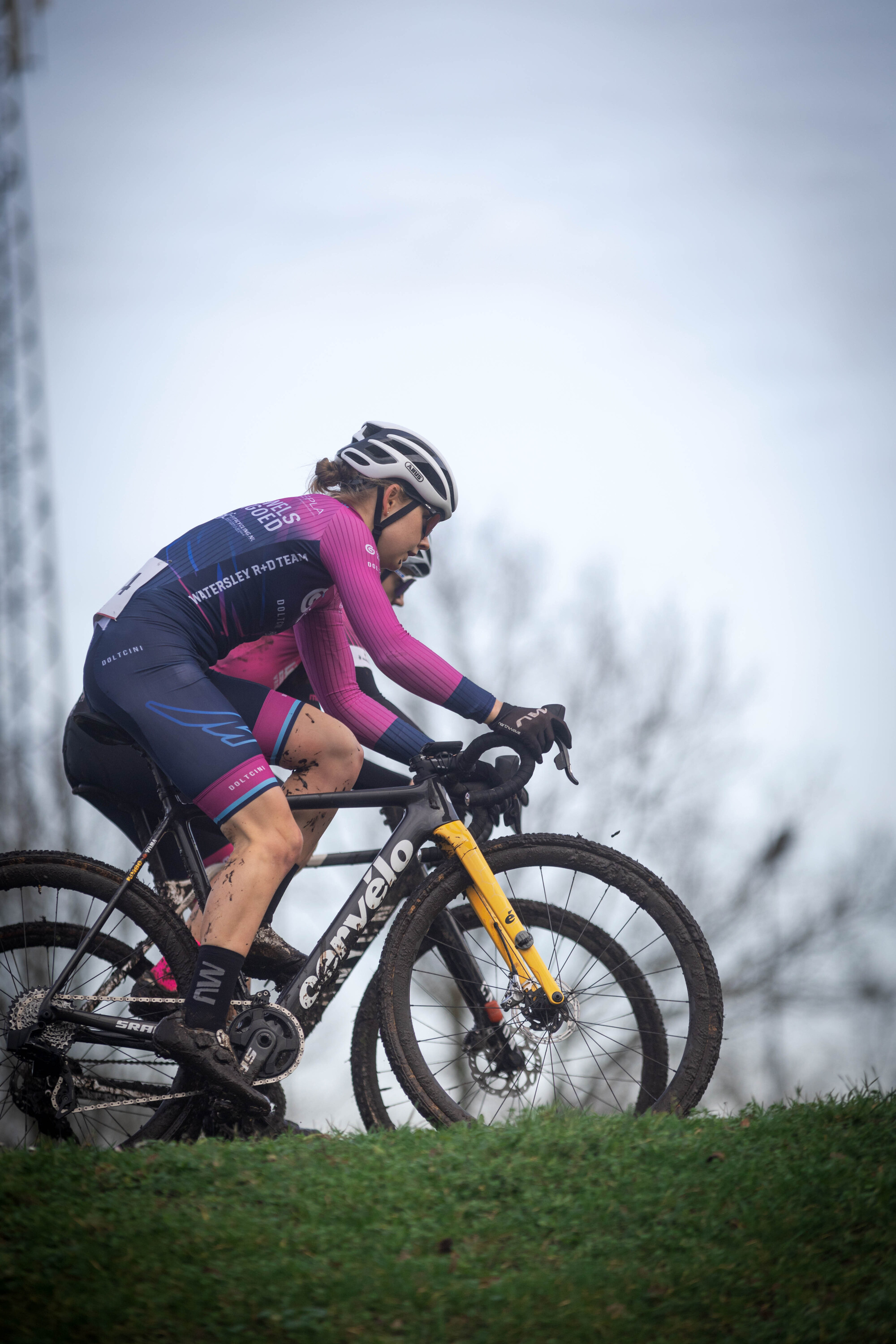 A woman wearing a black and pink jersey is riding a bicycle.