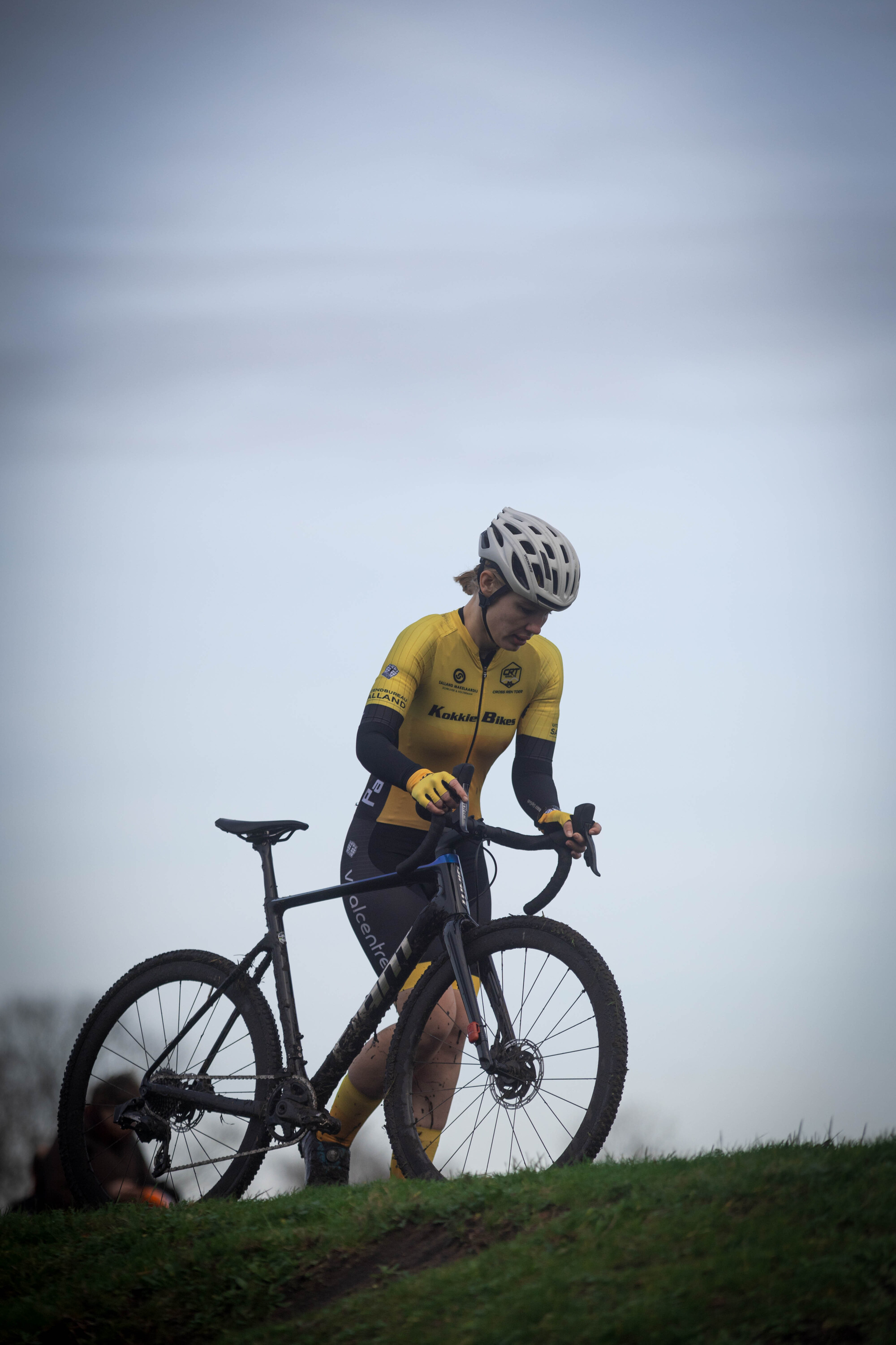 A cyclist in yellow is riding a bike on a grassy hill.