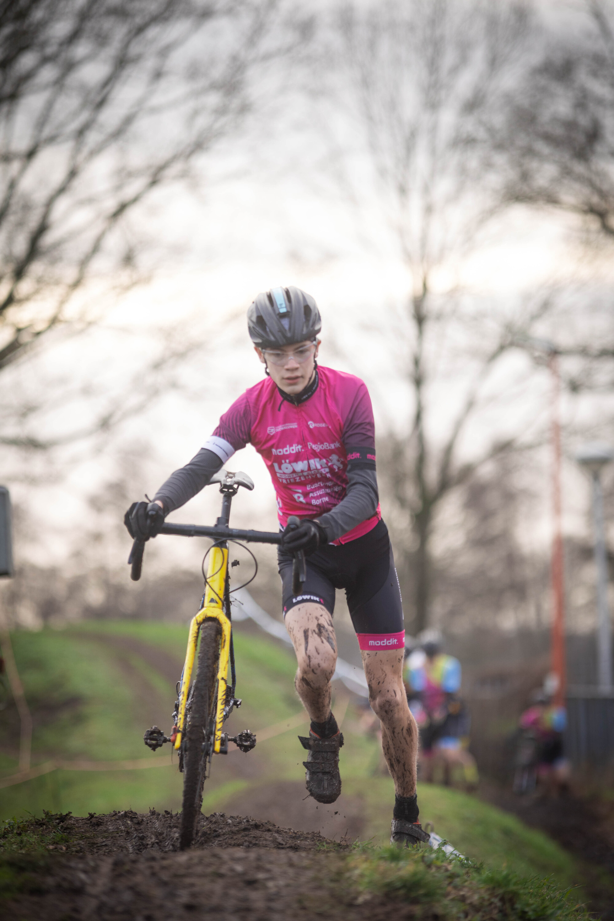 A young girl wearing a pink shirt and black shorts races on her yellow bicycle.