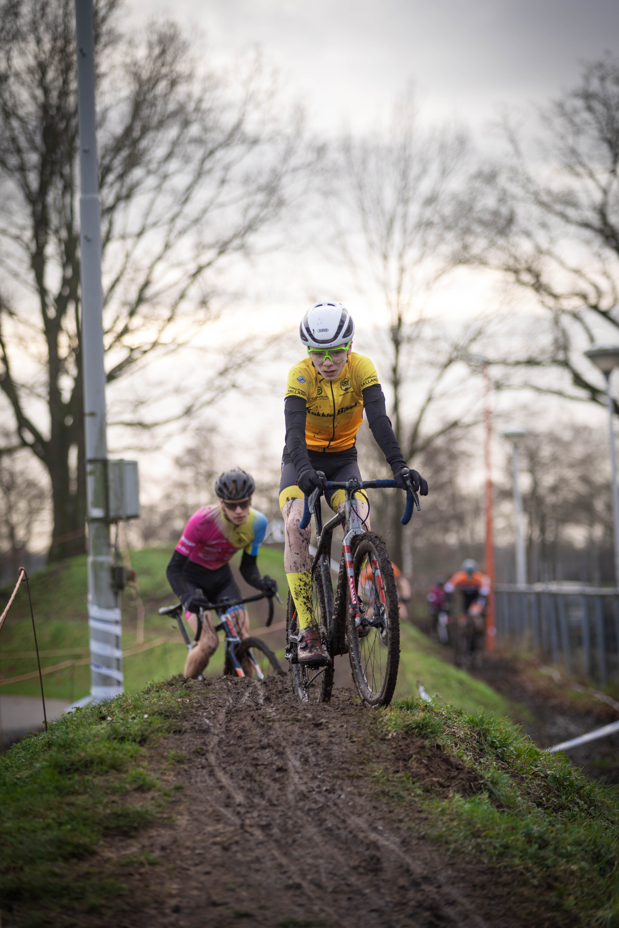 A cyclist in a yellow jersey is leading a group of cyclists on a dirt path.