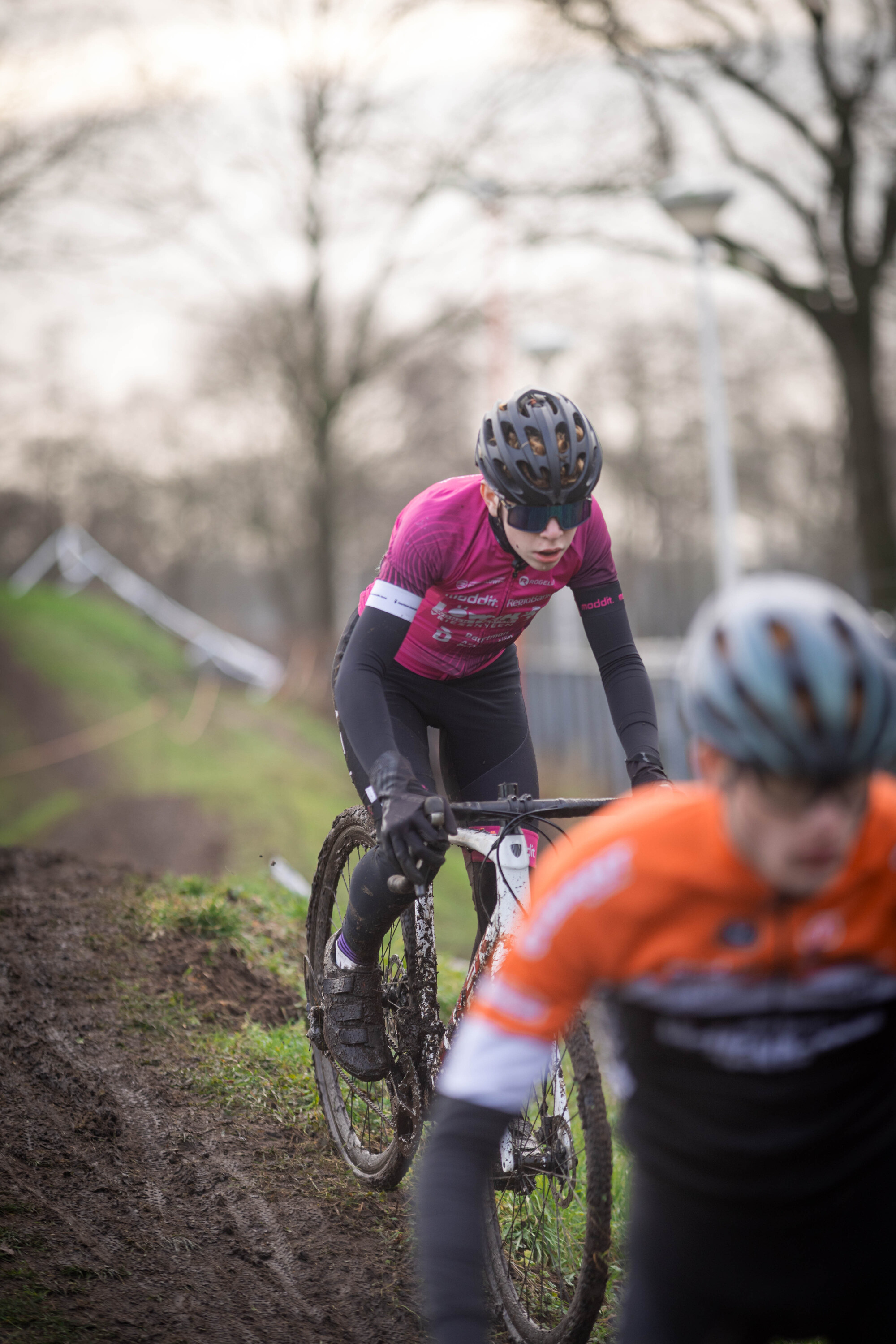 Two cyclists are on a dirt track and they both have blue helmets.