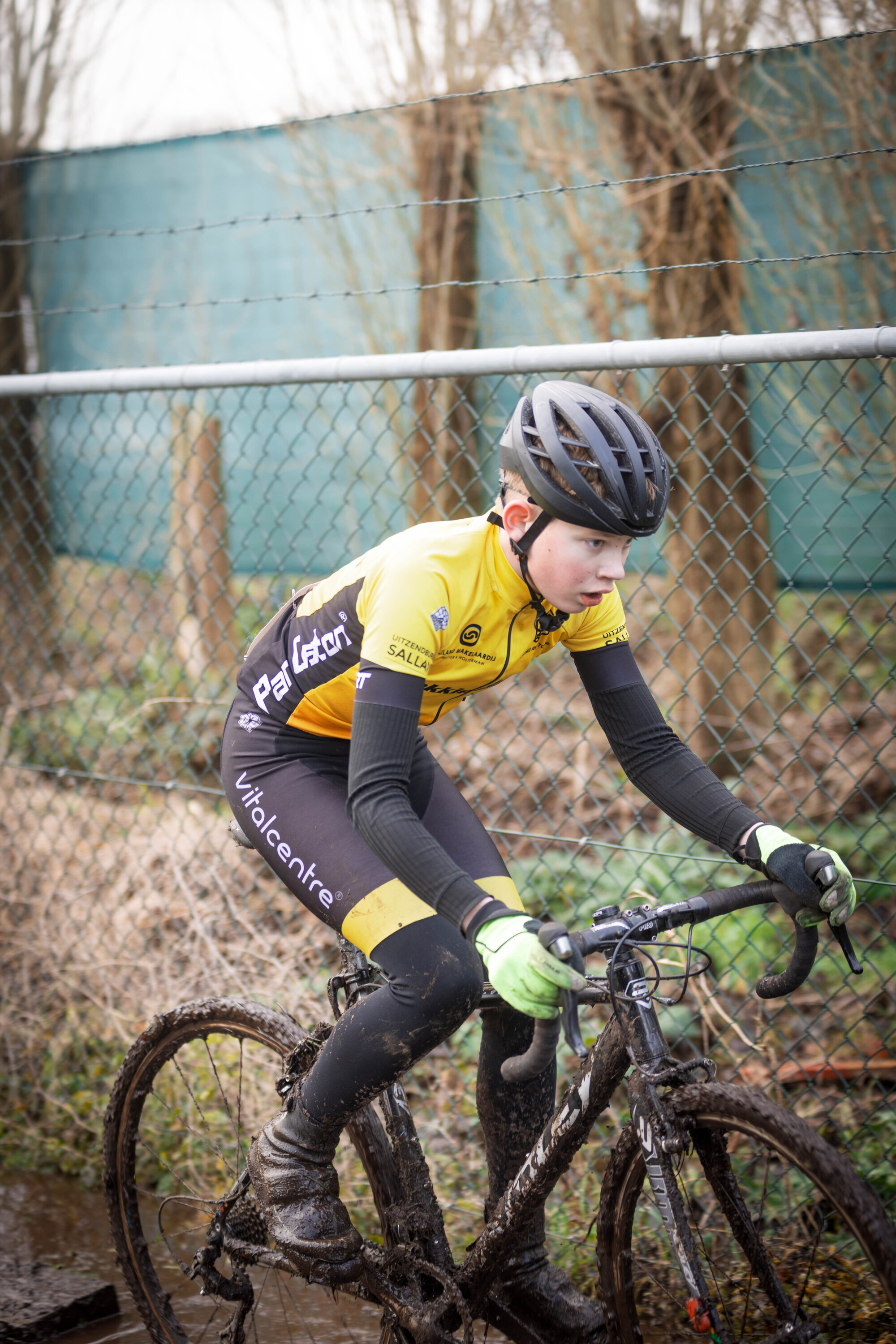 A cyclist on a dirty track wearing black and yellow clothing.