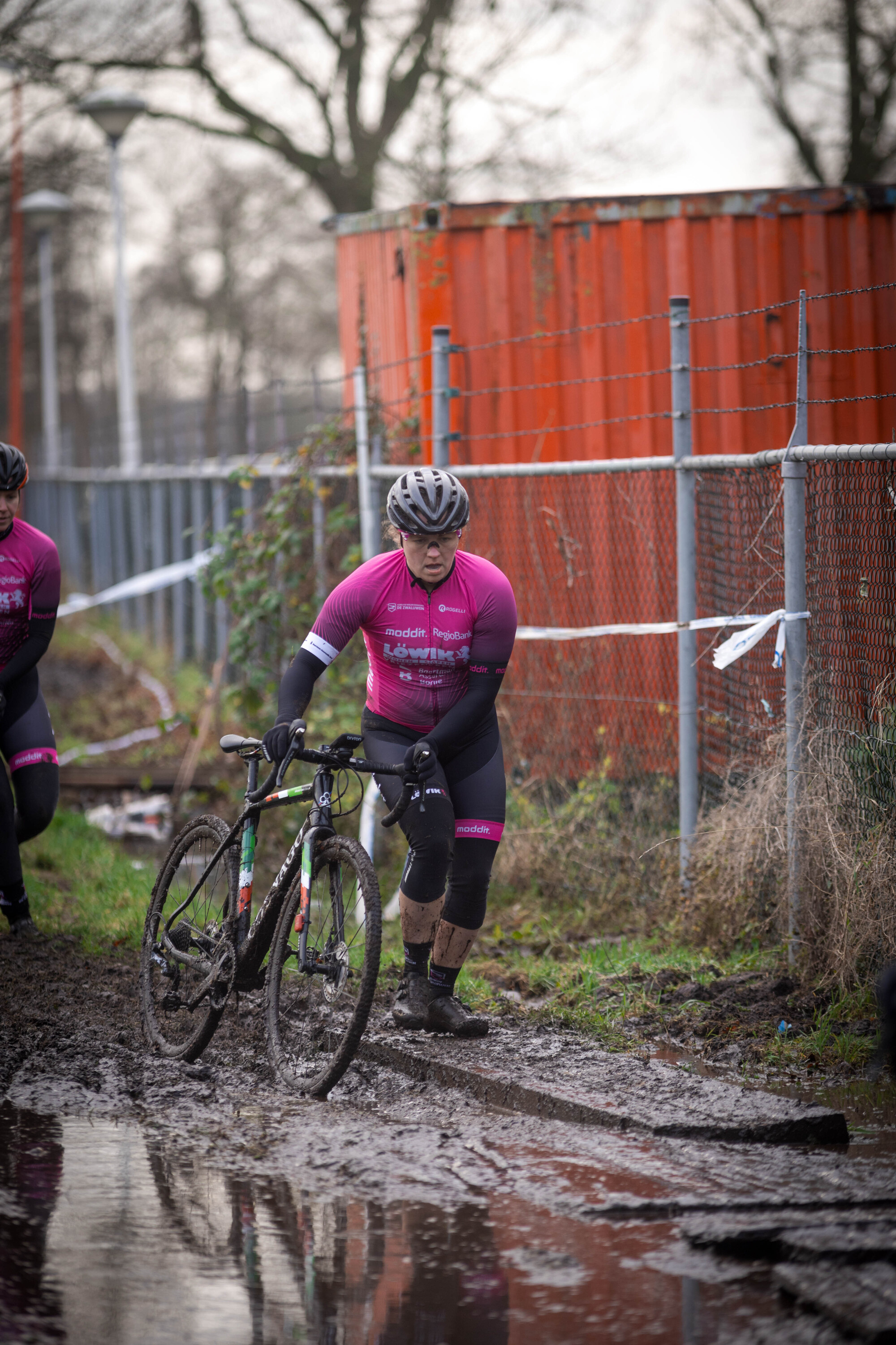 Cyclocross players wearing pink and black riding in mud.