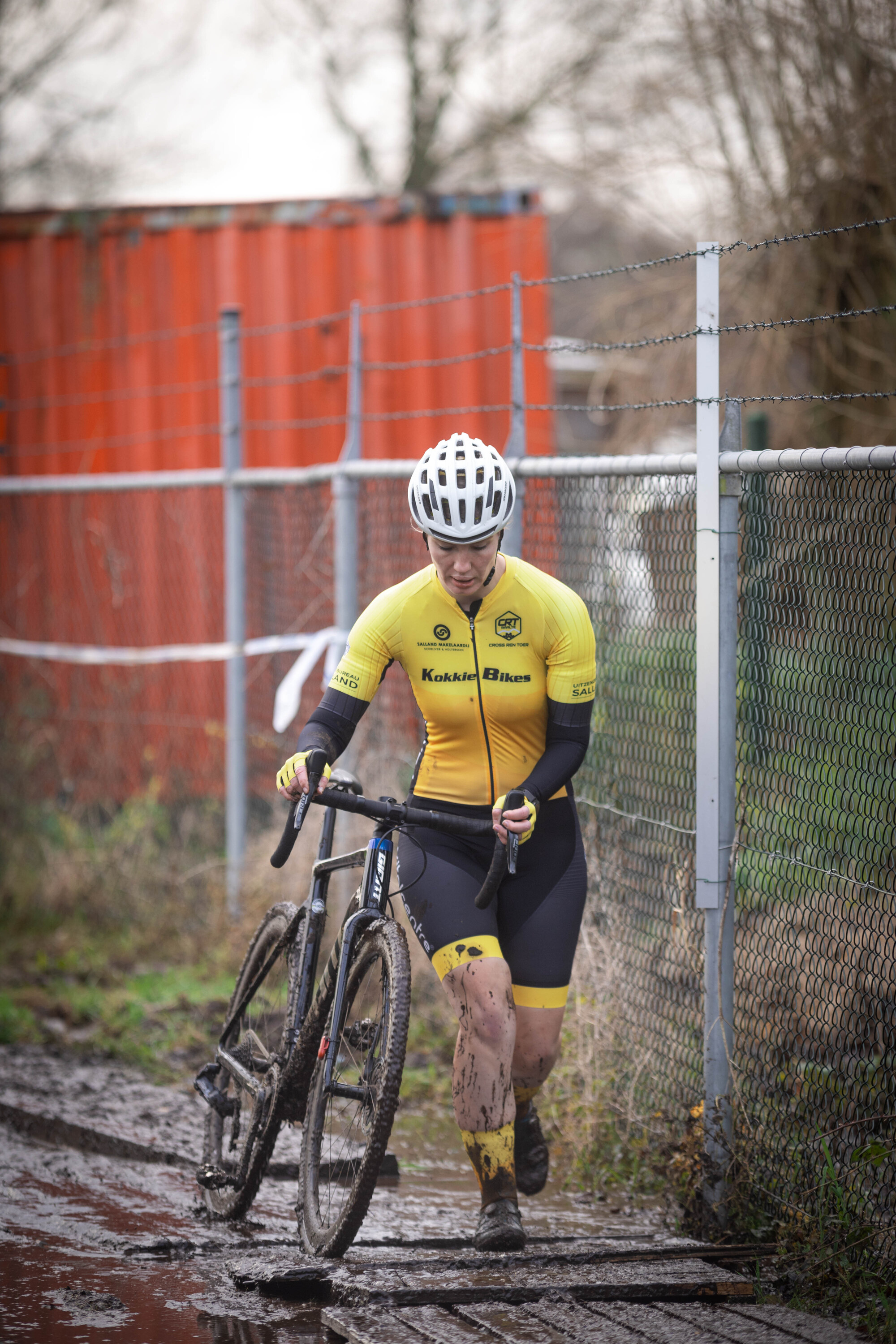 A cyclist wearing a yellow and black jersey is riding down a muddy path.