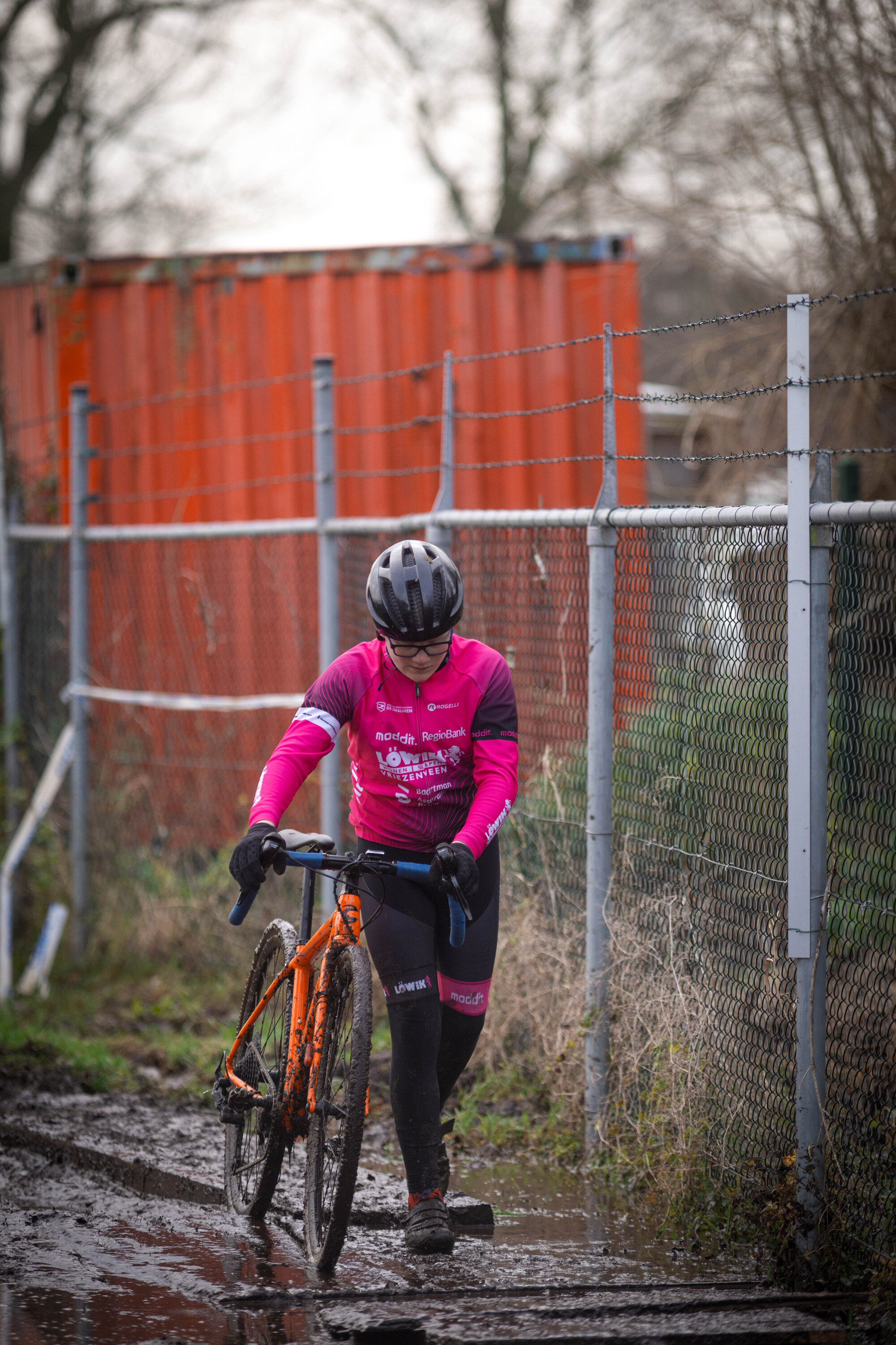 A person riding a bike in the rain, wearing pink and black.