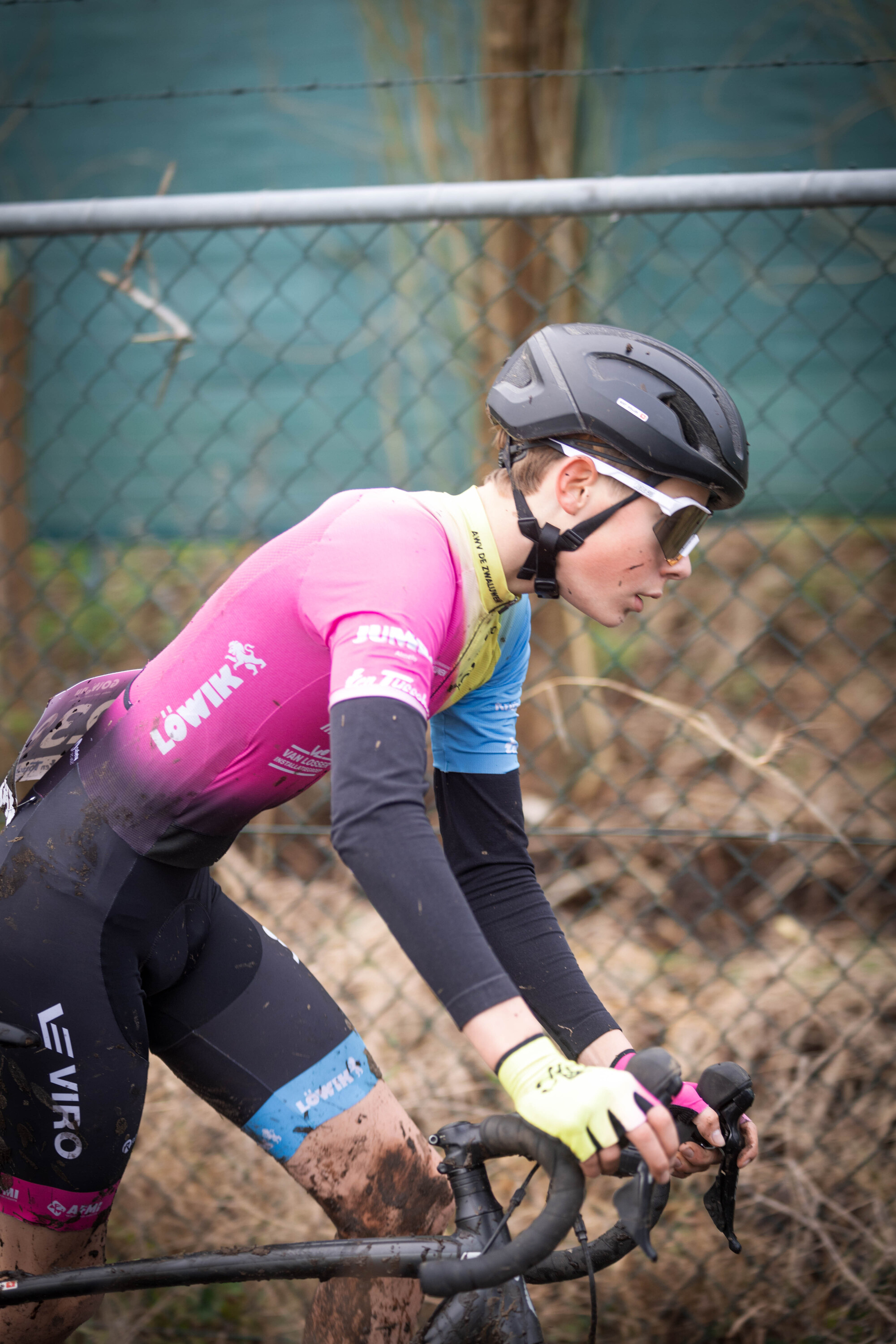 A young lady wearing a pink jersey and black bike pants is riding her mountain bike in mud.