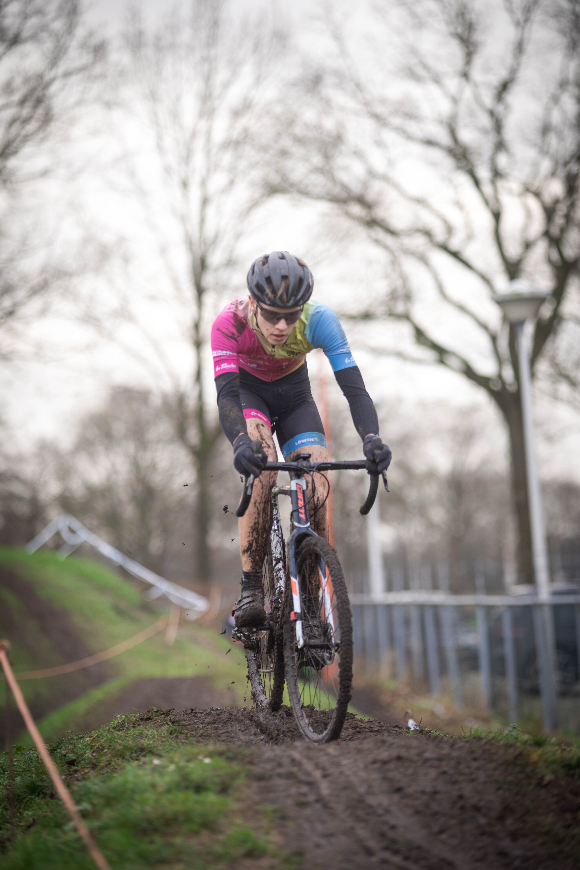 A person wearing a blue and pink jacket rides a mountain bike down an incline.