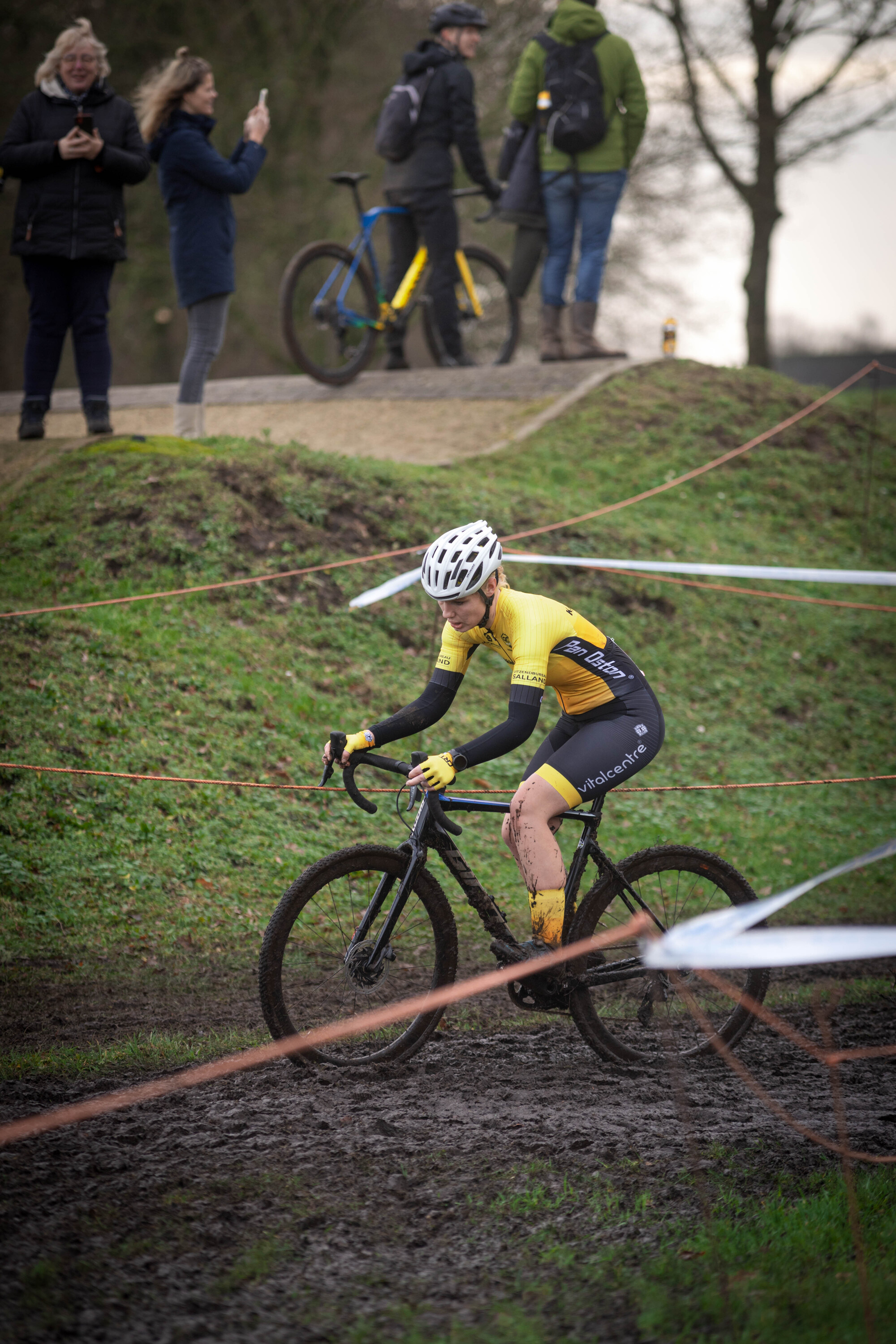 A man is riding a bicycle on a course with 9 other people standing and watching.