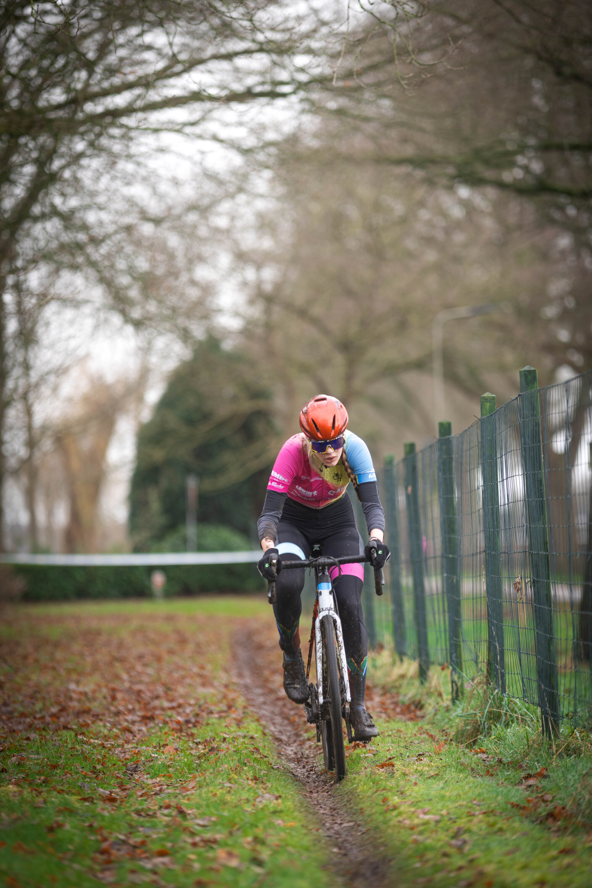 A woman is riding a bicycle on the grass beside a fence.