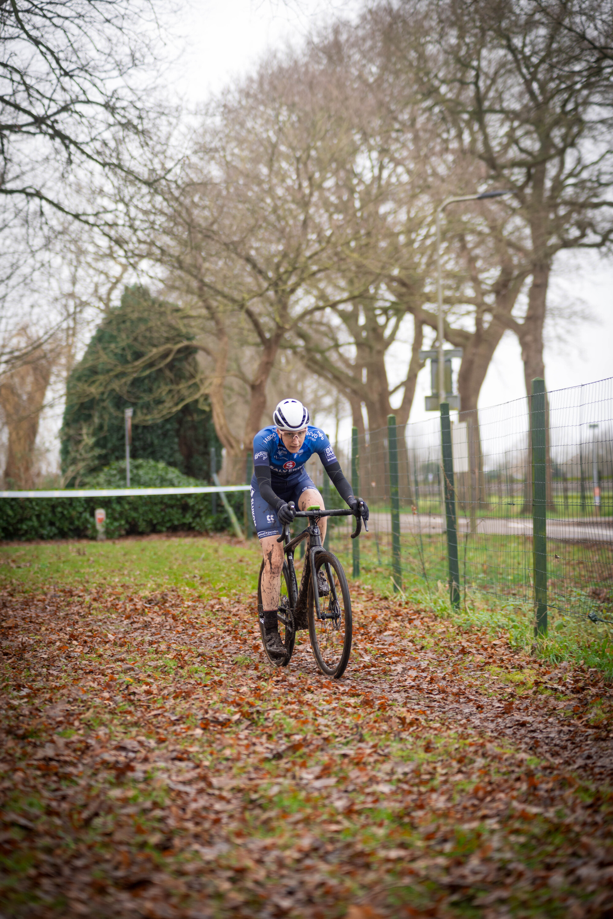 A cyclist in a blue and white jersey rides a bicycle down an unpaved road through autumn.