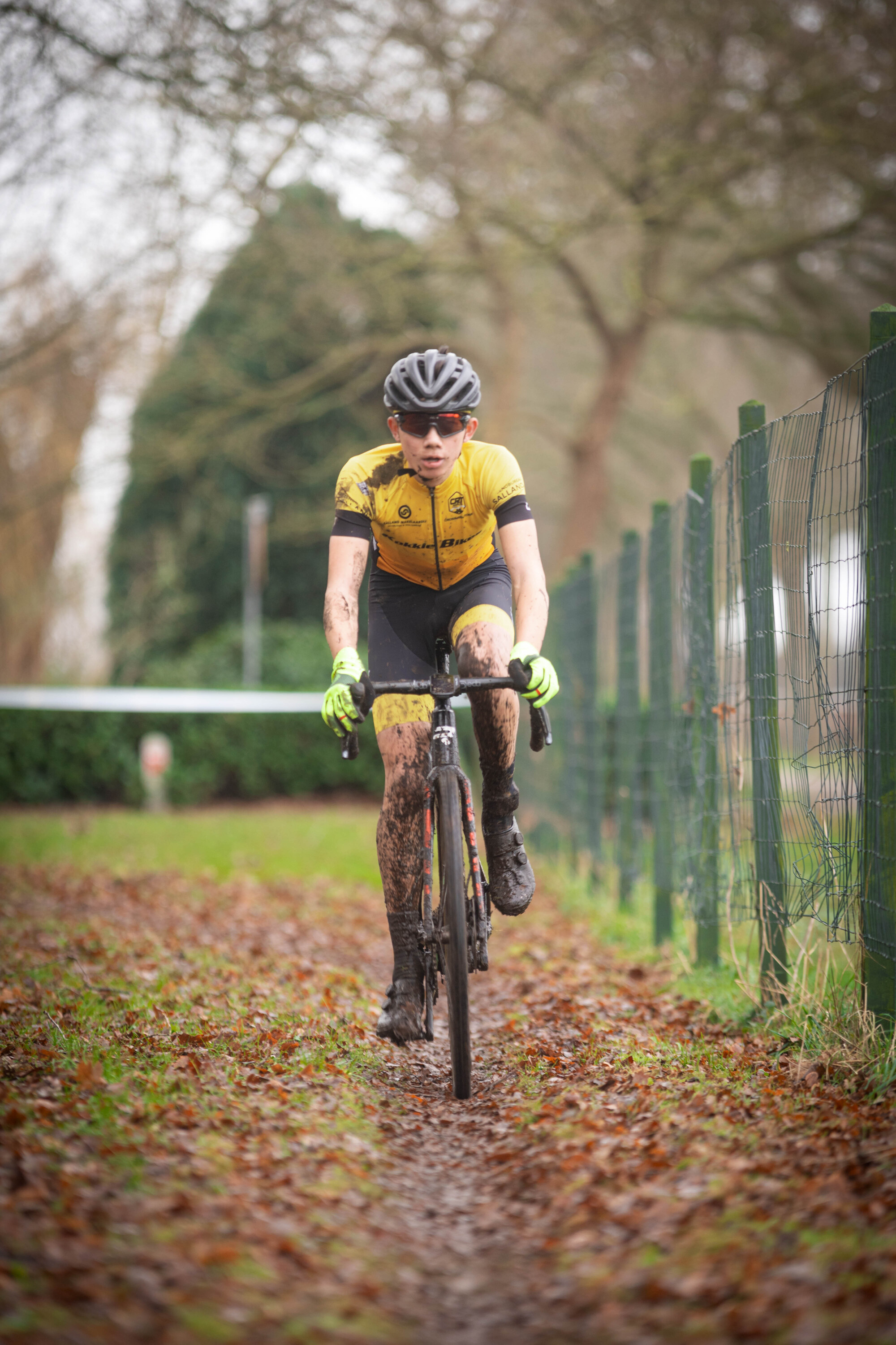 A man in a yellow jersey is riding a bicycle through muddy grass and leaves.