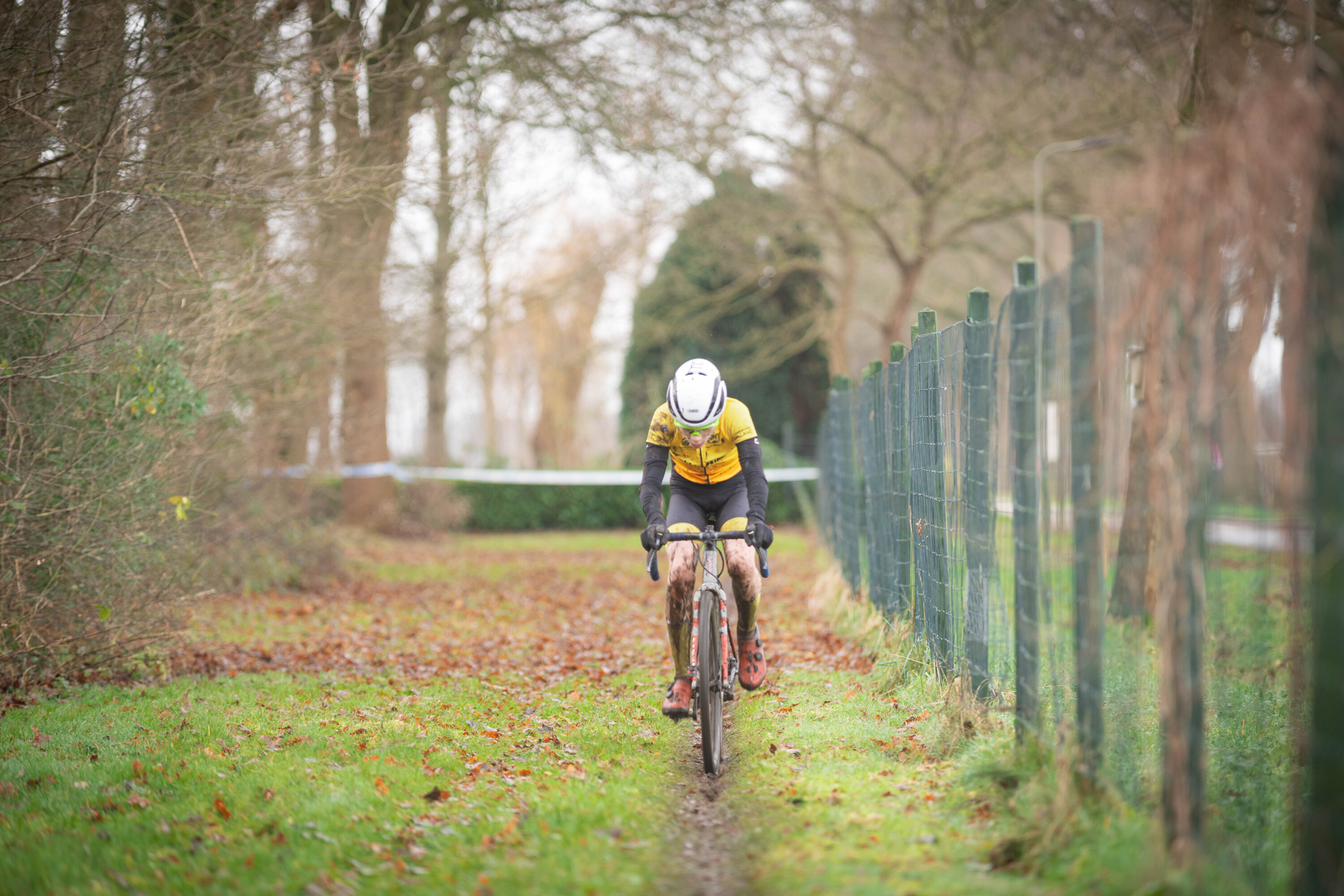 A cyclist in a yellow jersey and white helmet is riding a bike down a path through a forest.