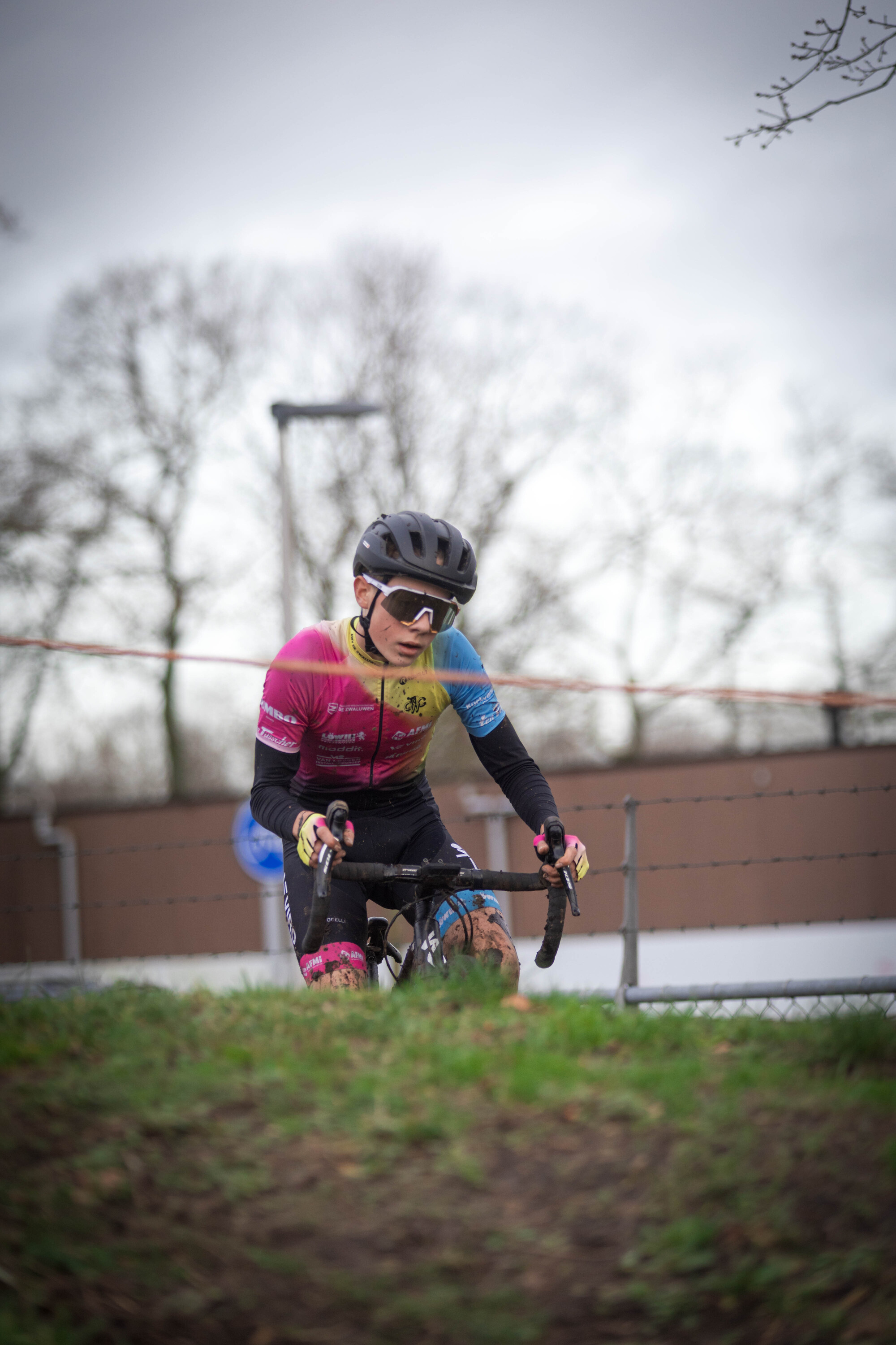 A young person in a pink and blue shirt is riding a bike on grass.