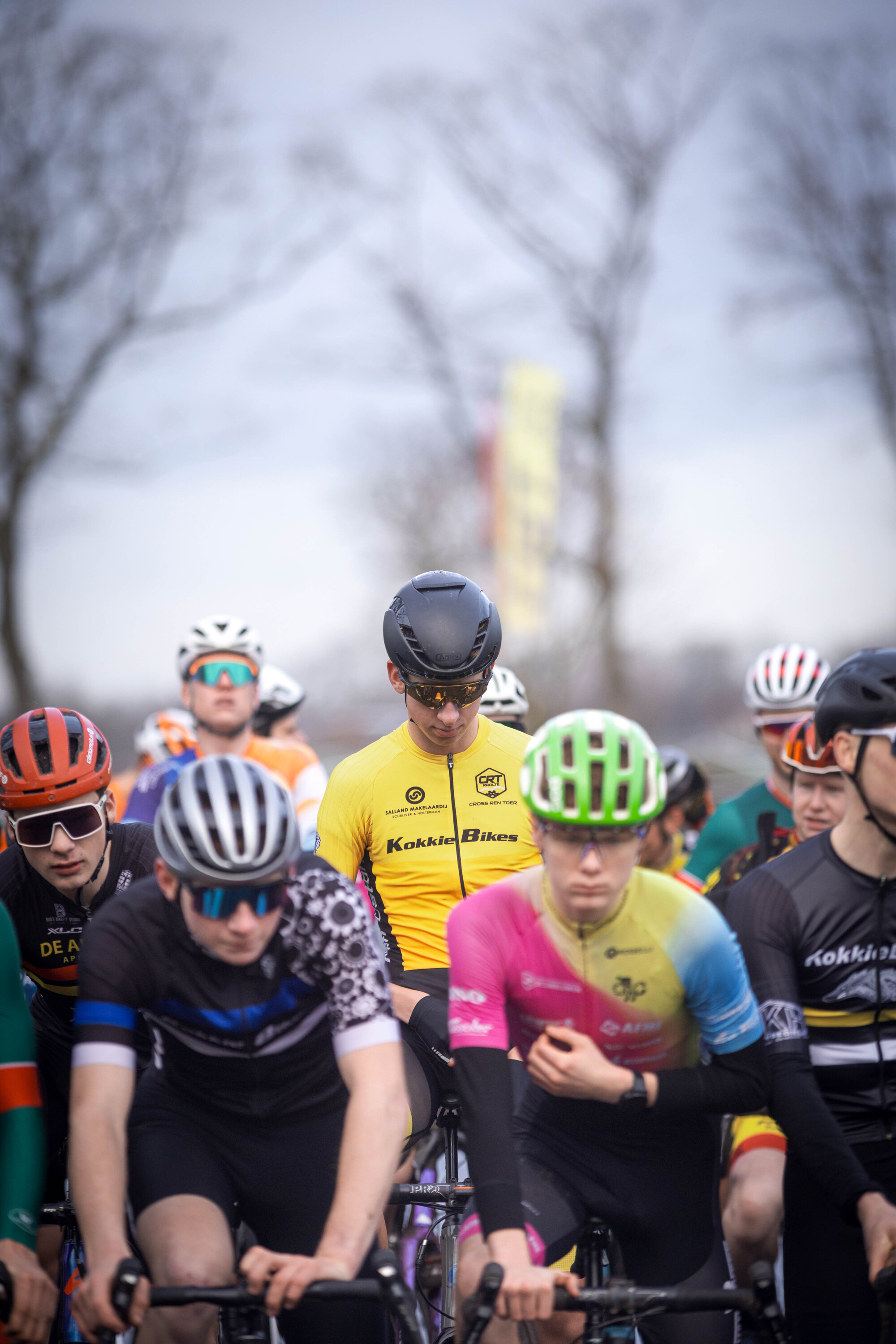 Cyclists in a group wearing different colored shirts, and helmets are racing through the streets.