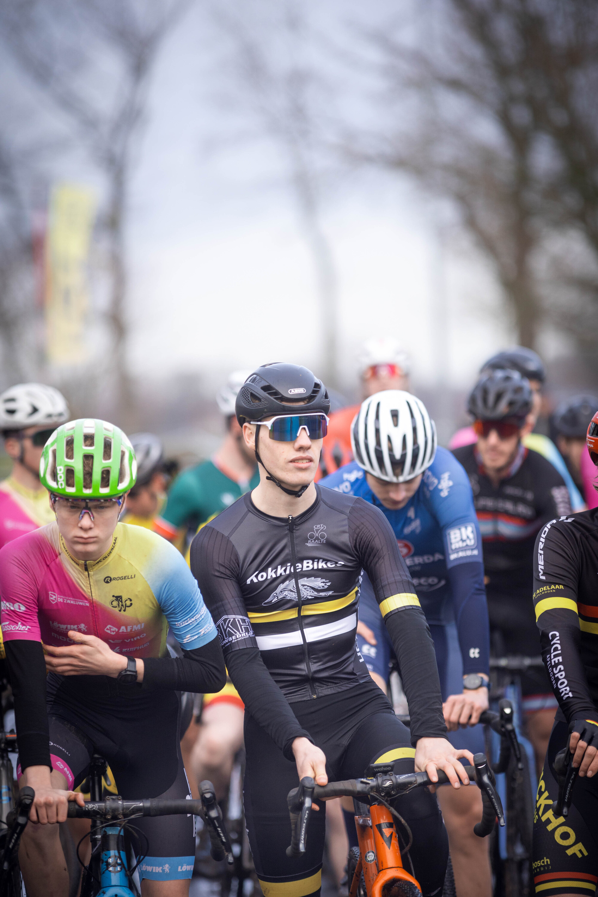 A group of cyclists in black and yellow suits with one on the left wearing a green helmet.