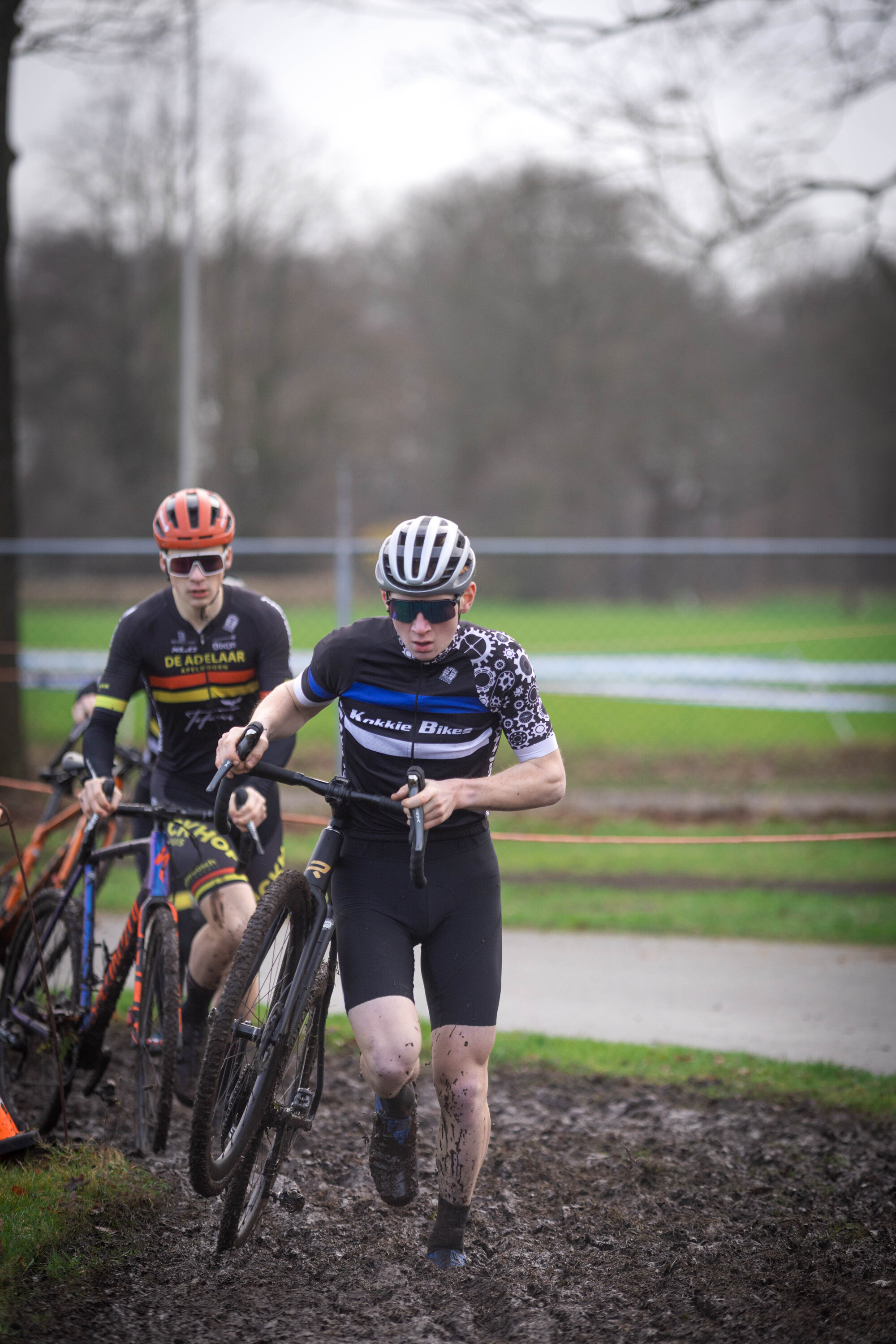 Two cyclists racing in the rain with one wearing black and white with "GOW Raalte" on the front.