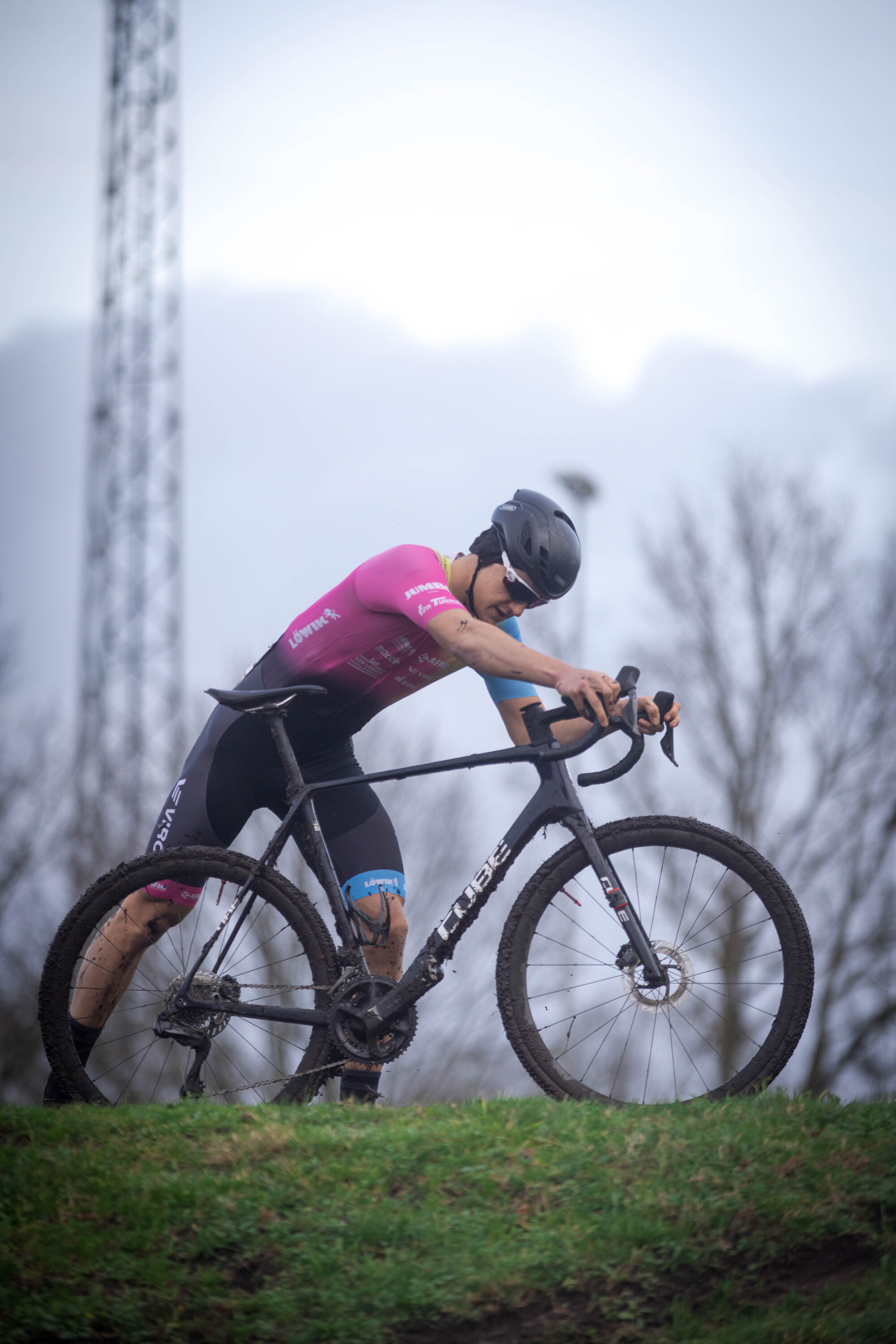 A man in a black helmet is riding a mountain bike with a pink shirt that says Cyclocross.