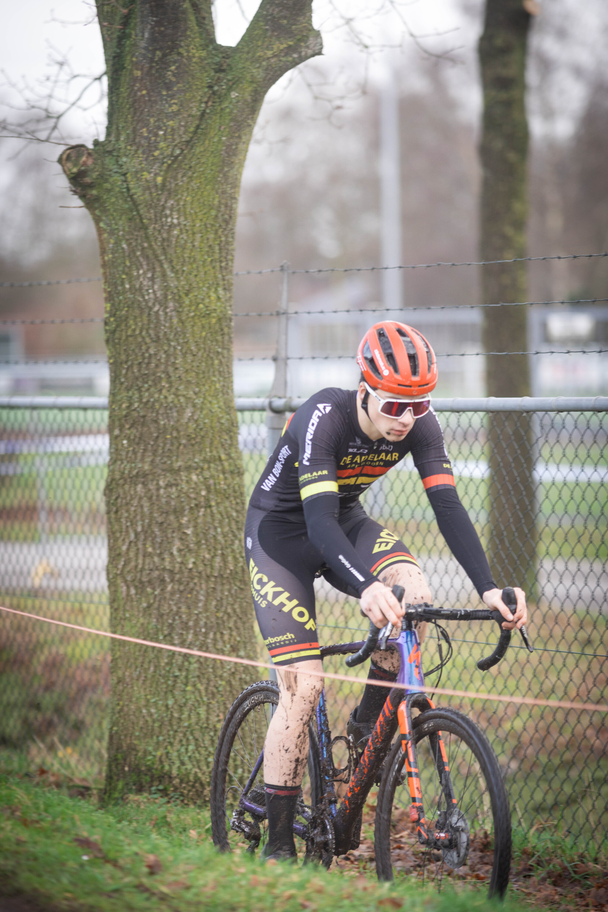 A man wearing a black shirt and orange helmet riding a bike.