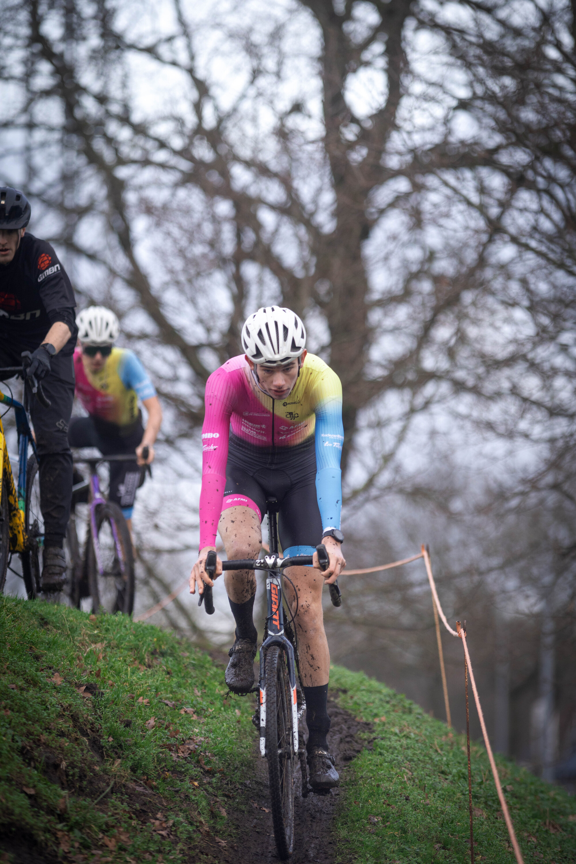 Three people are riding their bikes on a hill. One is wearing a pink jersey with the number 6 on it.