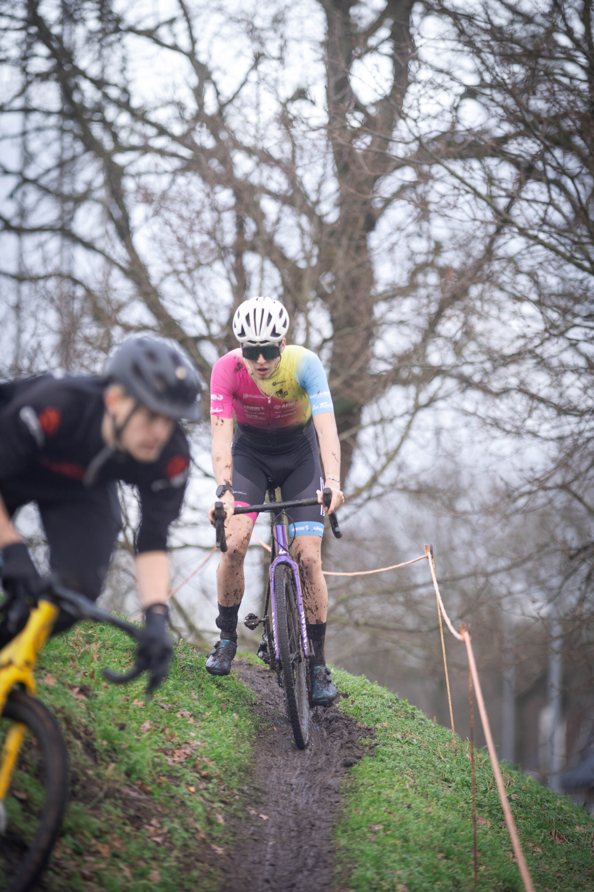 Two bicyclists race down a hill, wearing helmets and colorful jerseys.