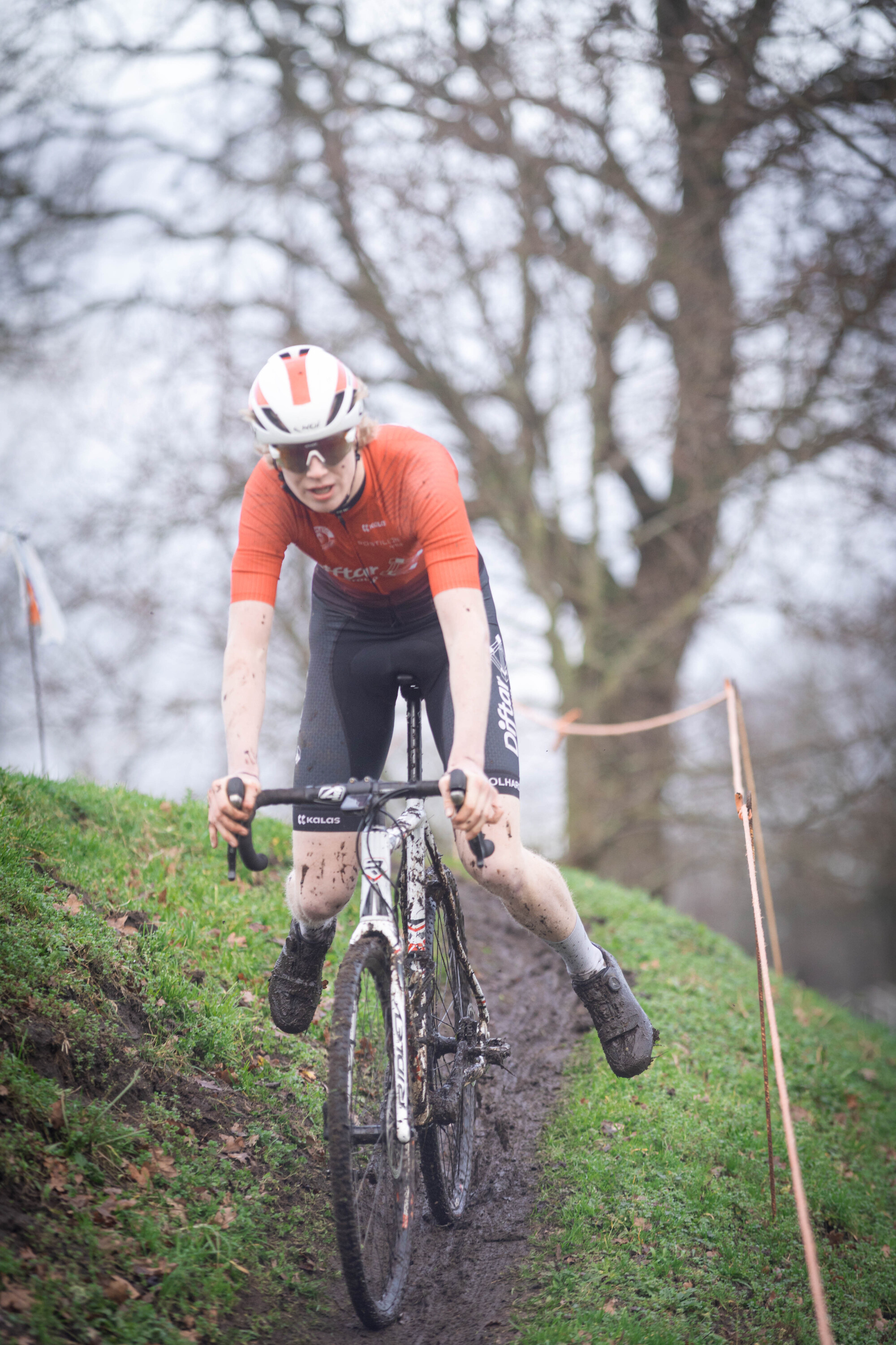 A person is cycling with a red shirt on and a red and white helmet.