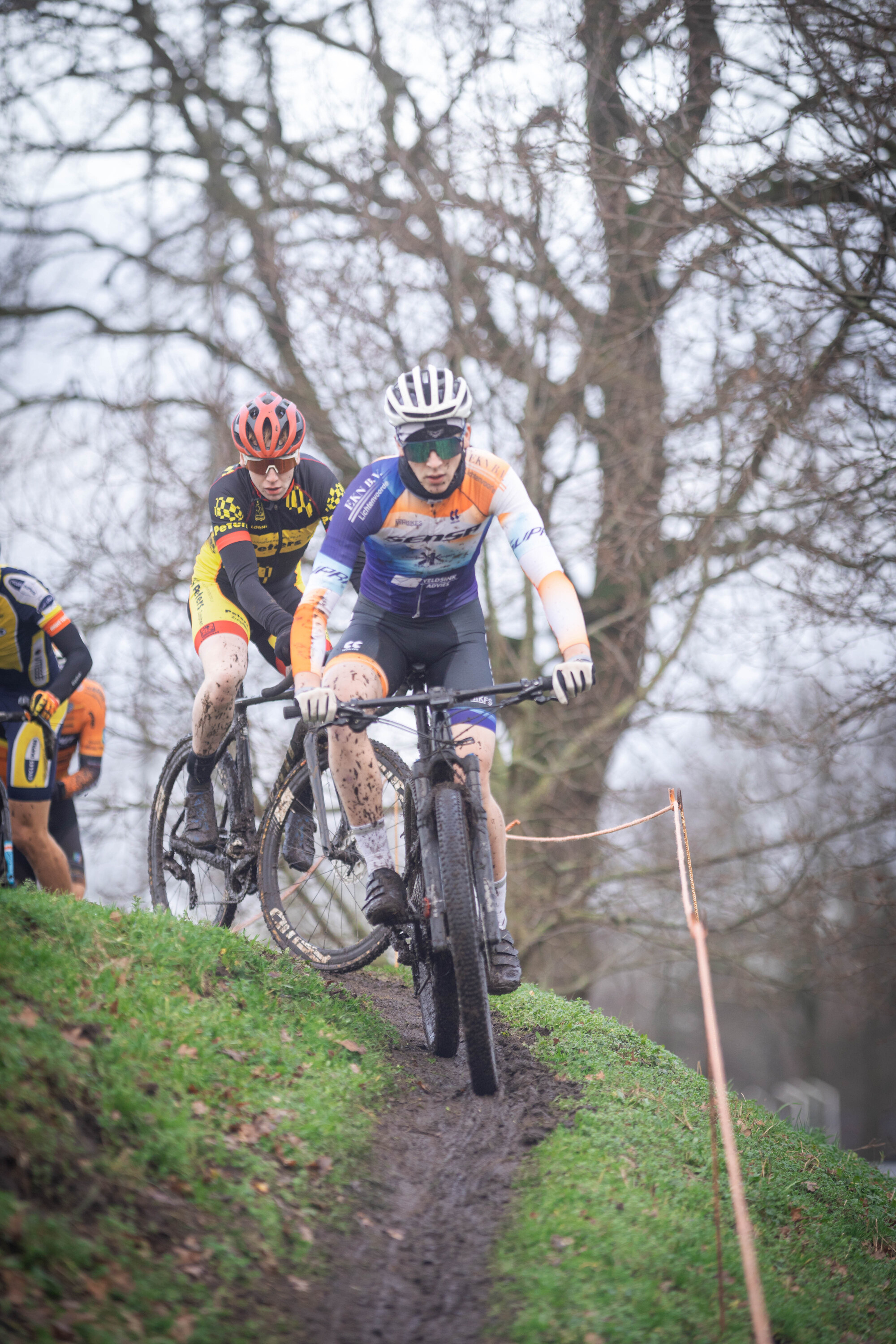 Two cyclists on a course, one with an orange helmet and the other wearing a white helmet.