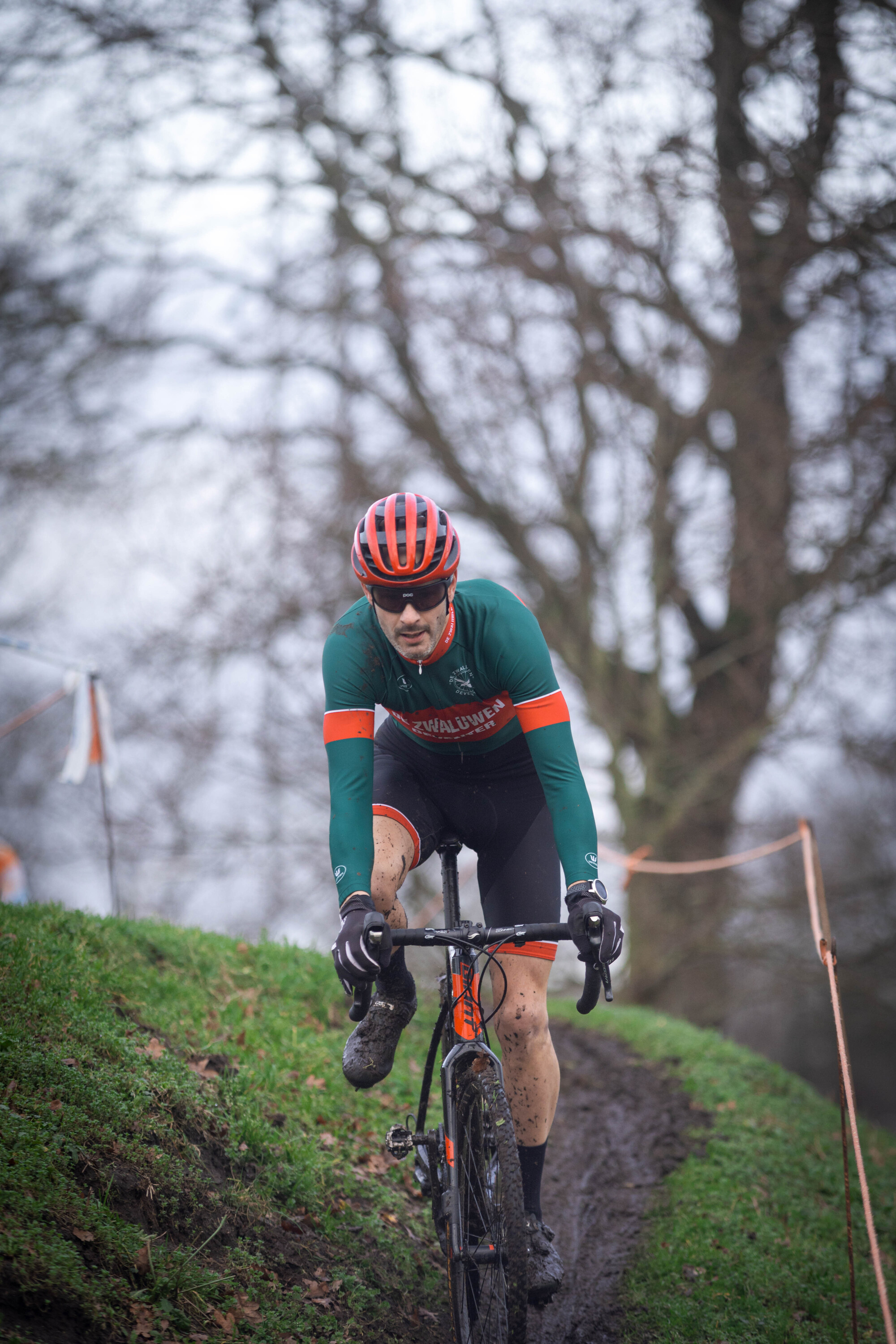 A person in a green and orange cycling outfit riding a bicycle down a hill.