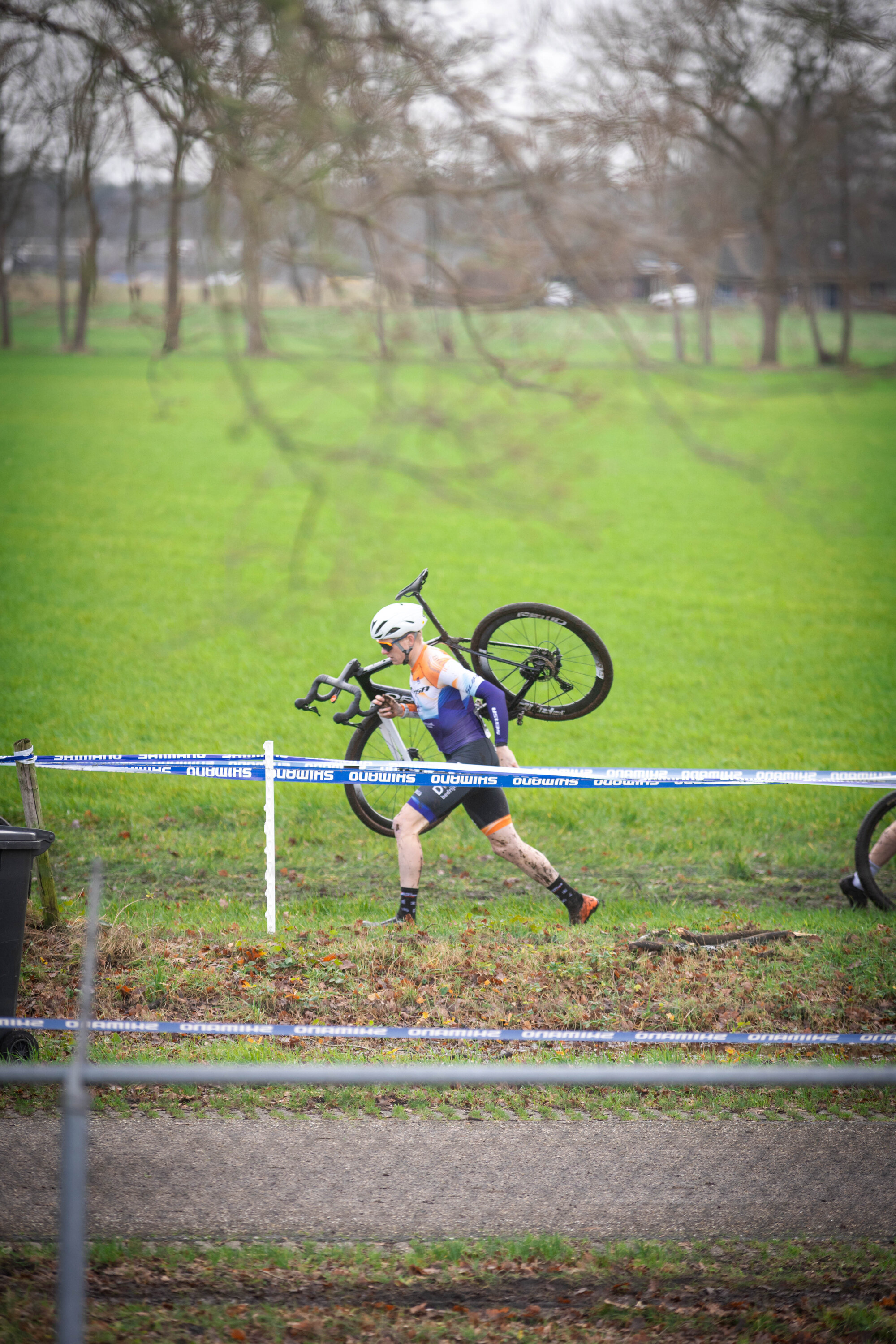 A cyclist is holding a bicycle while running on the grass.