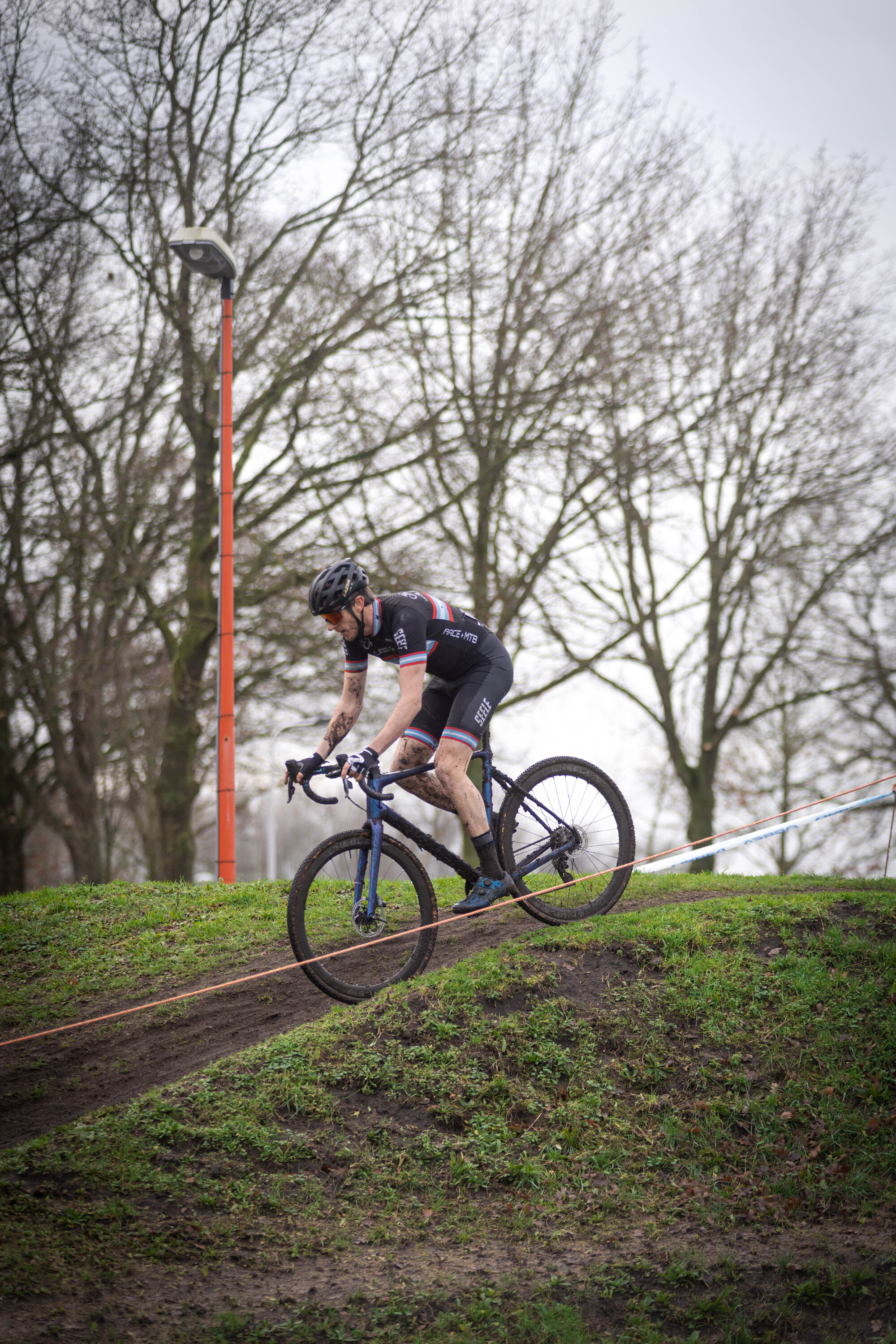 A man riding a bicycle on the side of a hill with trees and poles in the background.